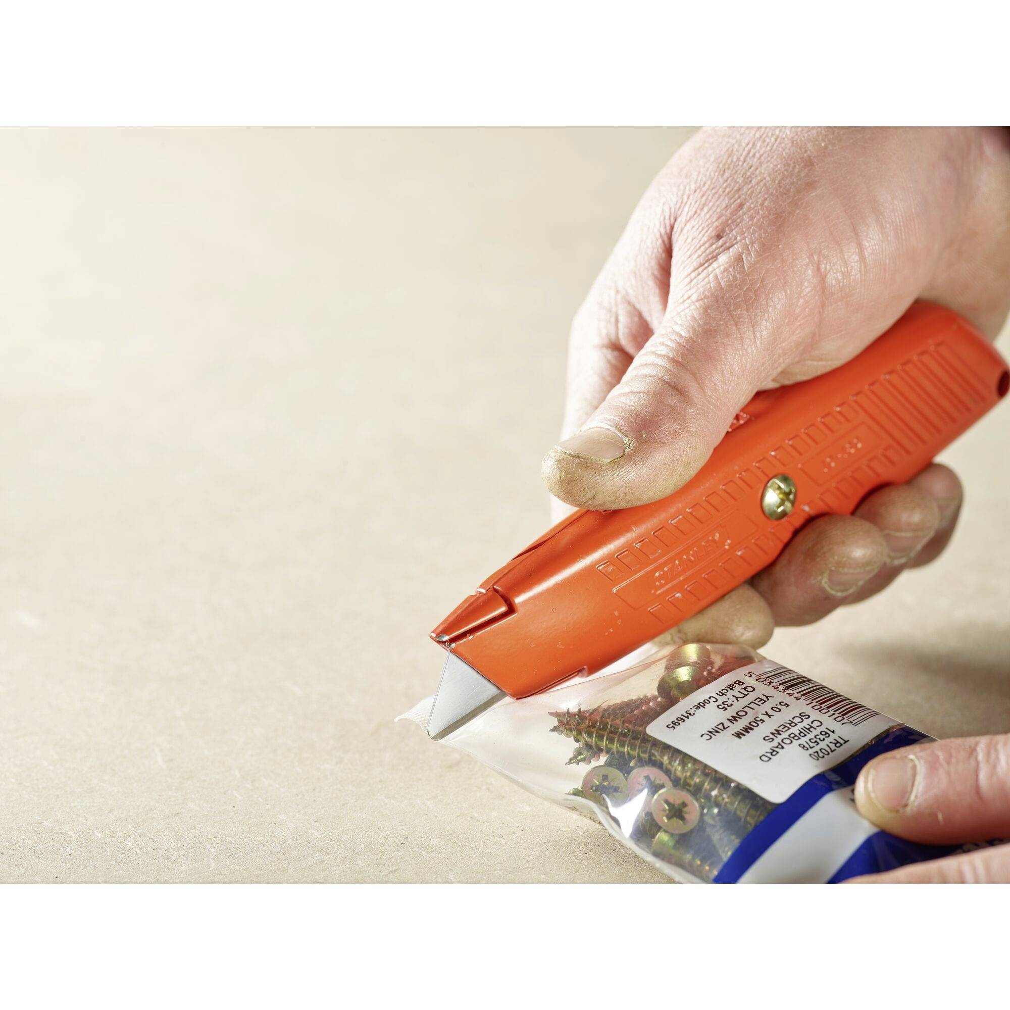 A hand is using a red cutting device to open a plastic bag containing screws.
