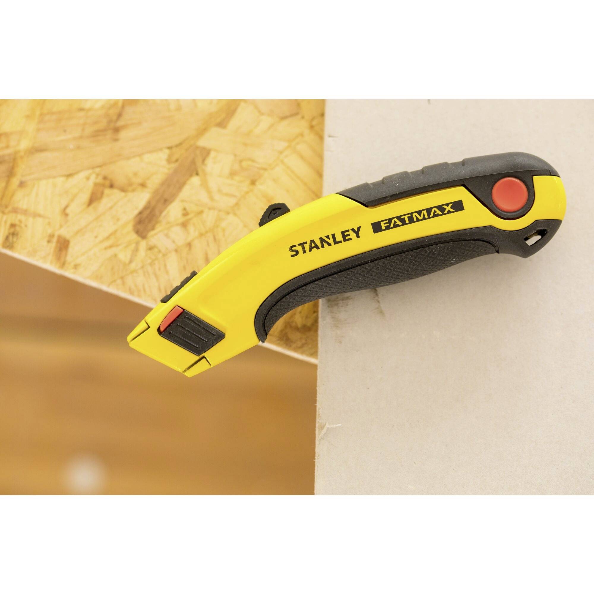 A yellow Stanley Fatmax utility knife lies on a wooden board; ergonomic design, used for cutting tasks.