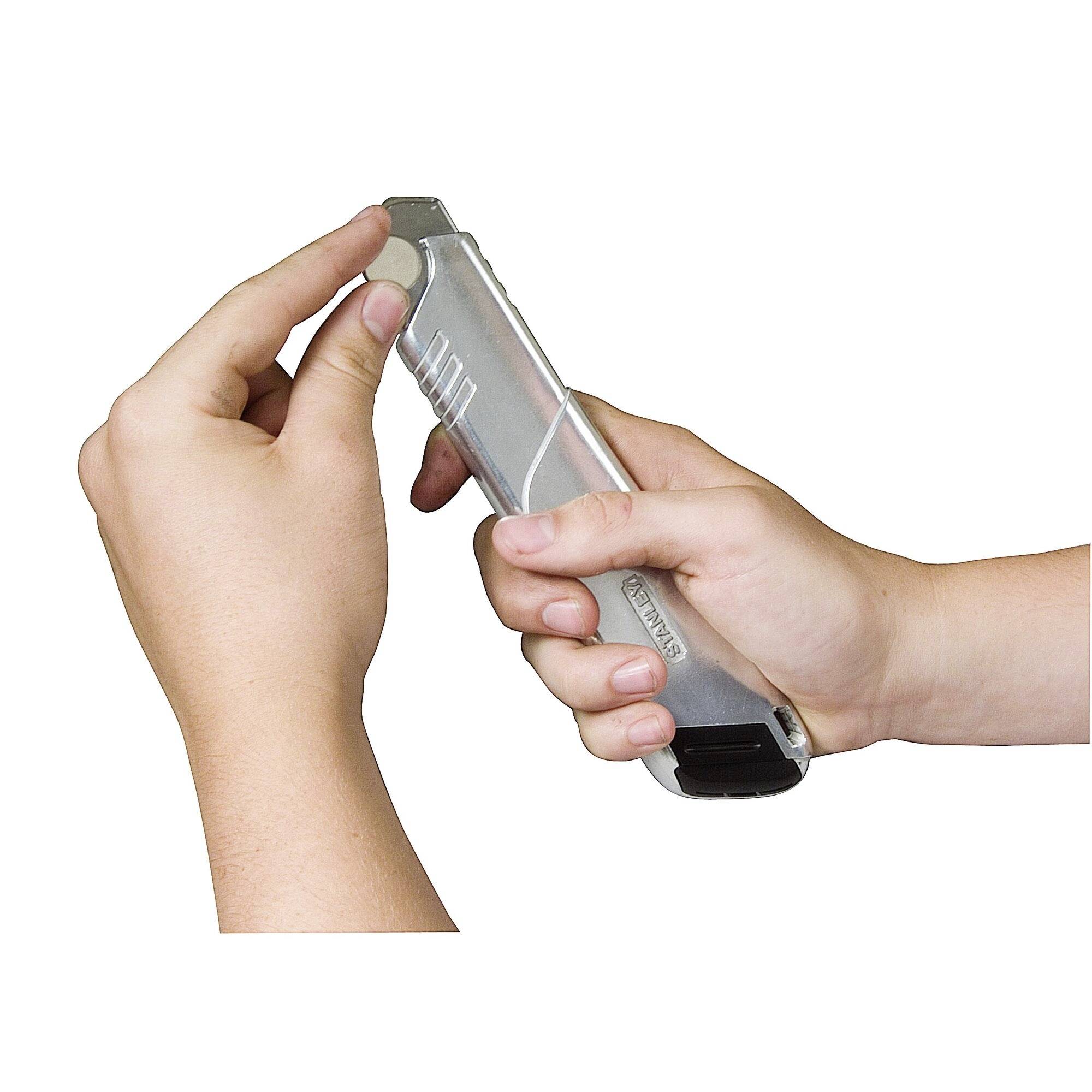 Two hands are holding a silver craft knife. One hand is pressing the slider to extend the blade.