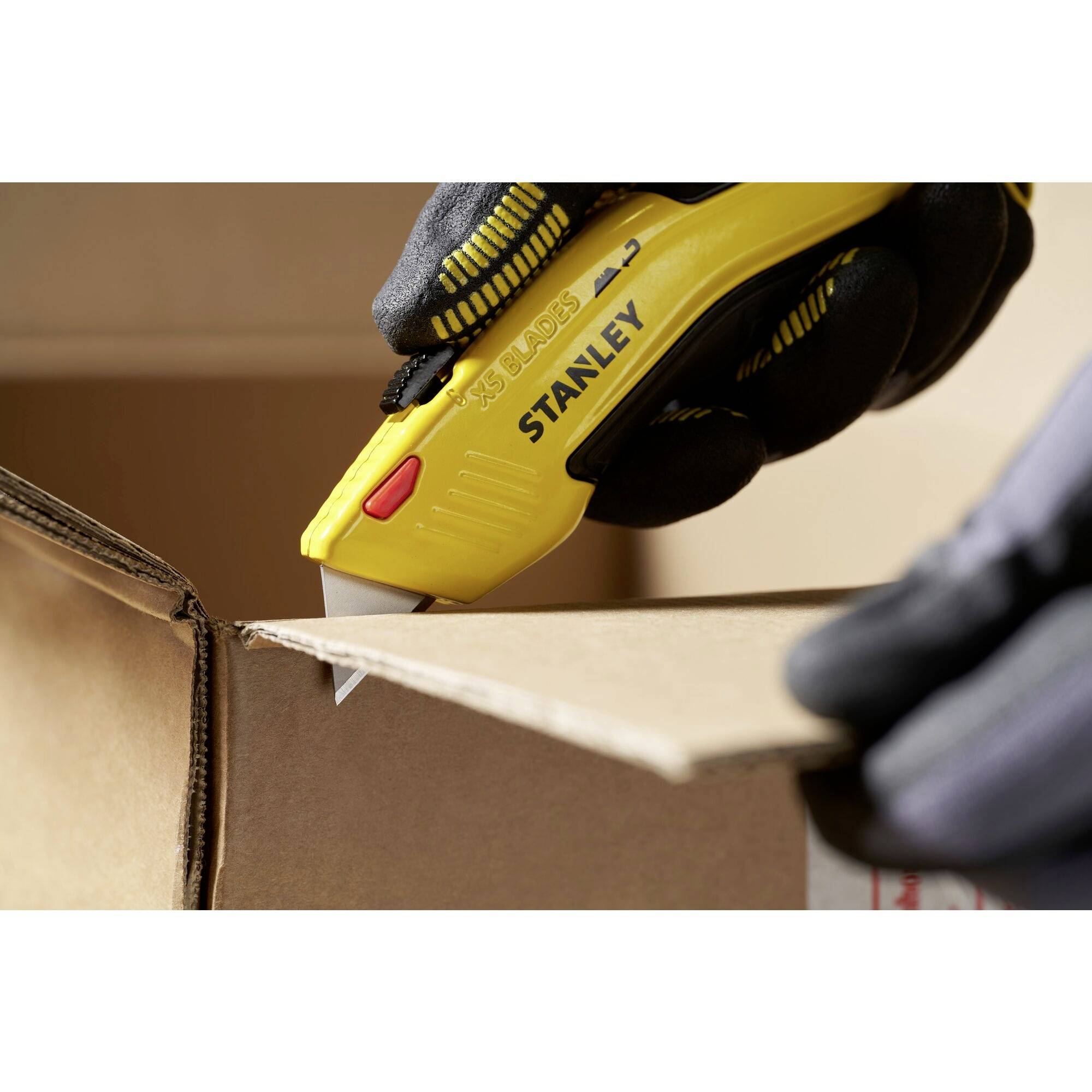 A person is carefully cutting open a cardboard box with a yellow Stanley utility knife.