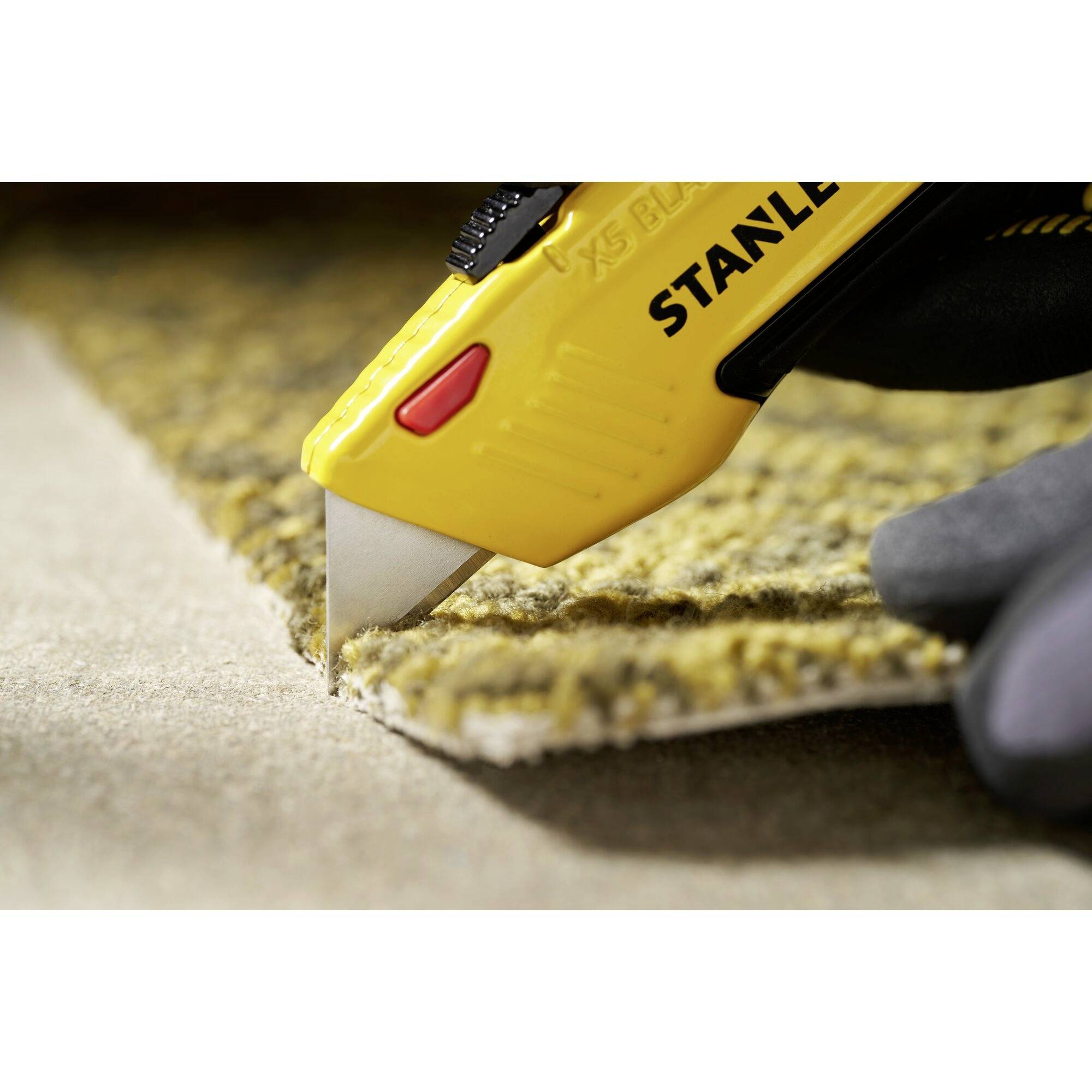A hand is cutting a yellow carpet with a yellow utility knife on a non-slip surface.