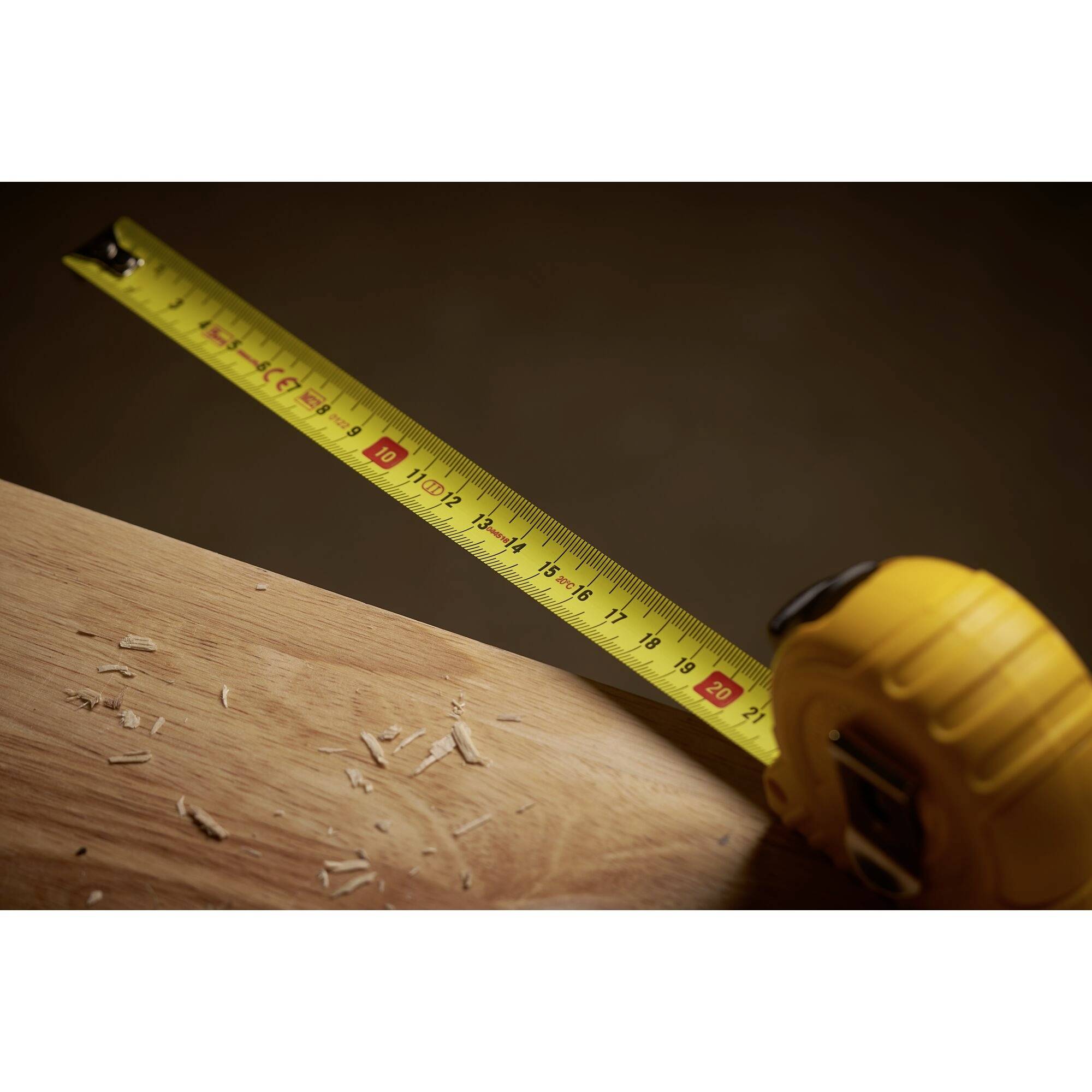 A yellow tape measure on a wooden table. The markings show up to 20 centimetres. Wood shavings are scattered nearby.