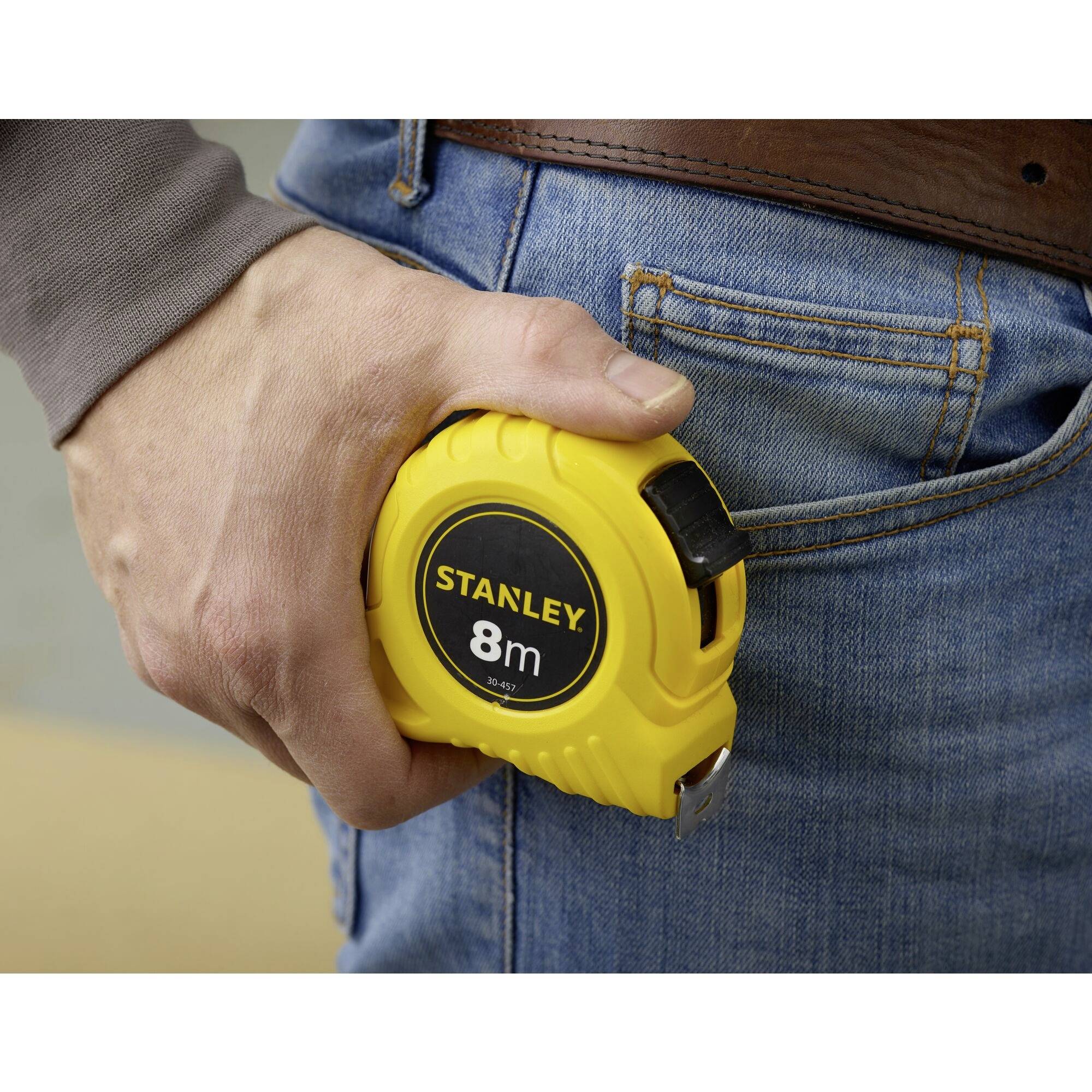 A person is holding a yellow 8m measuring tape in their hand and putting it into their jeans pocket.