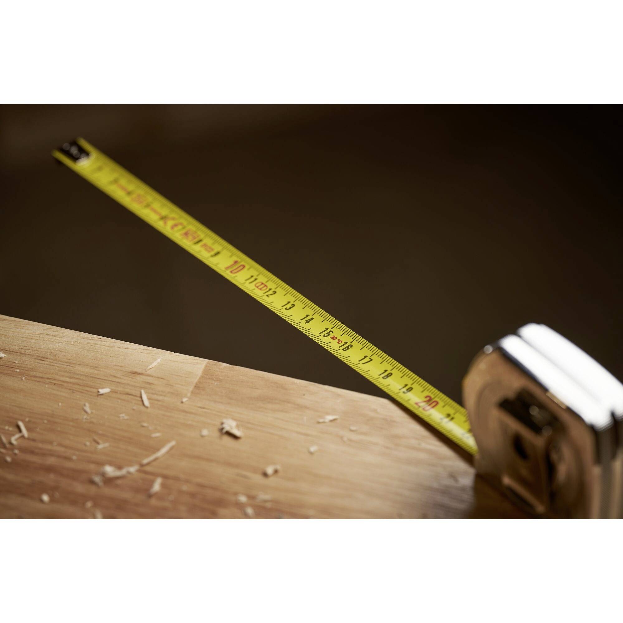 A yellow measuring tape lies on a wooden table with wood shavings. It shows a length of approximately one metre.