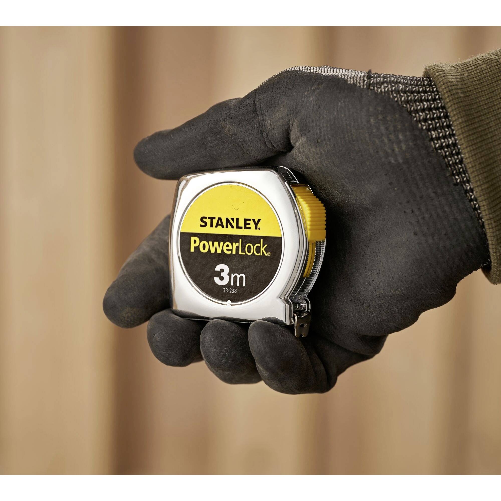 A hand holds a Stanley PowerLock tape measure. The tape measure has a yellow and silver surface and is suitable for precise measurements.