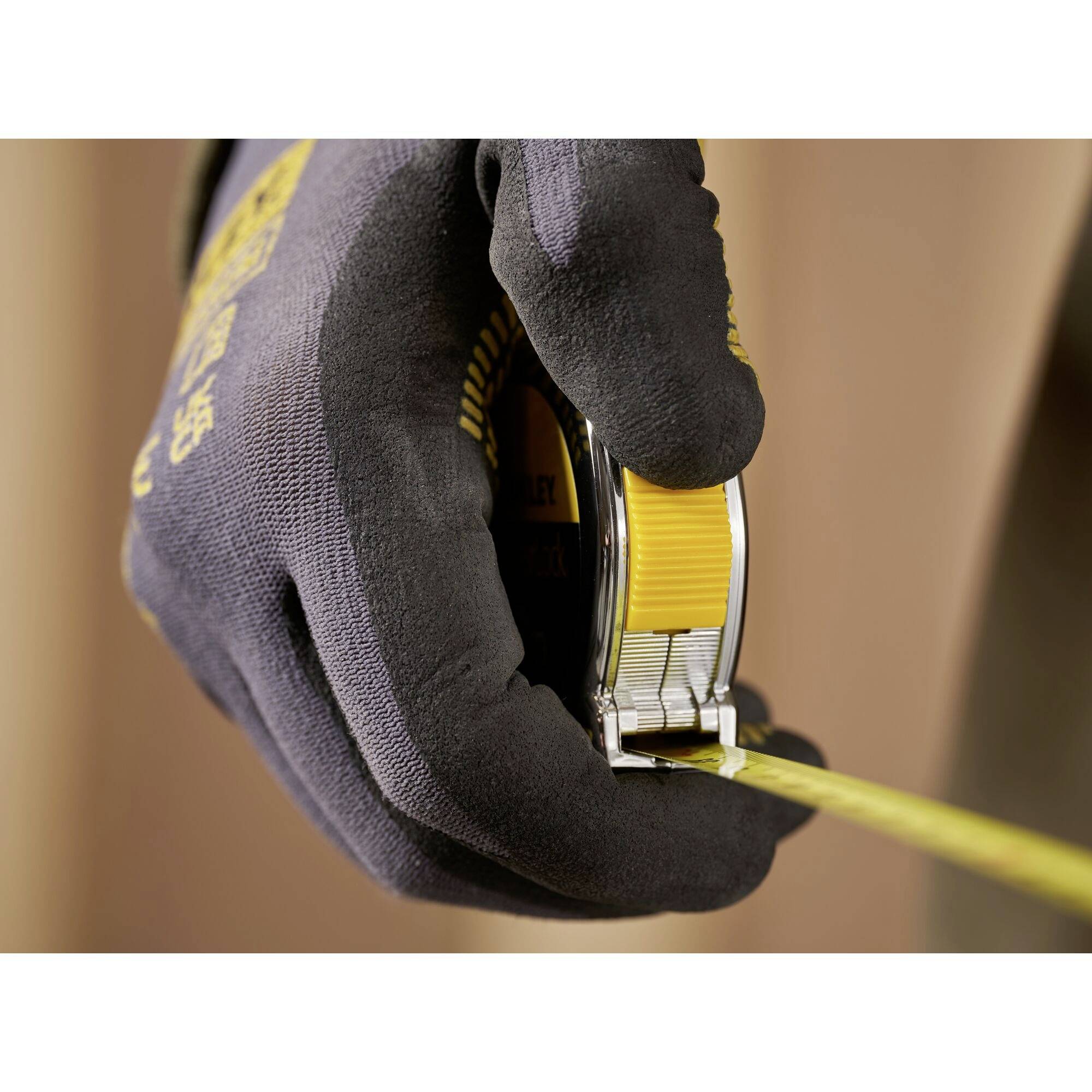 A hand wearing a black glove is holding a yellow measuring tape, which is being pulled out to measure a length.