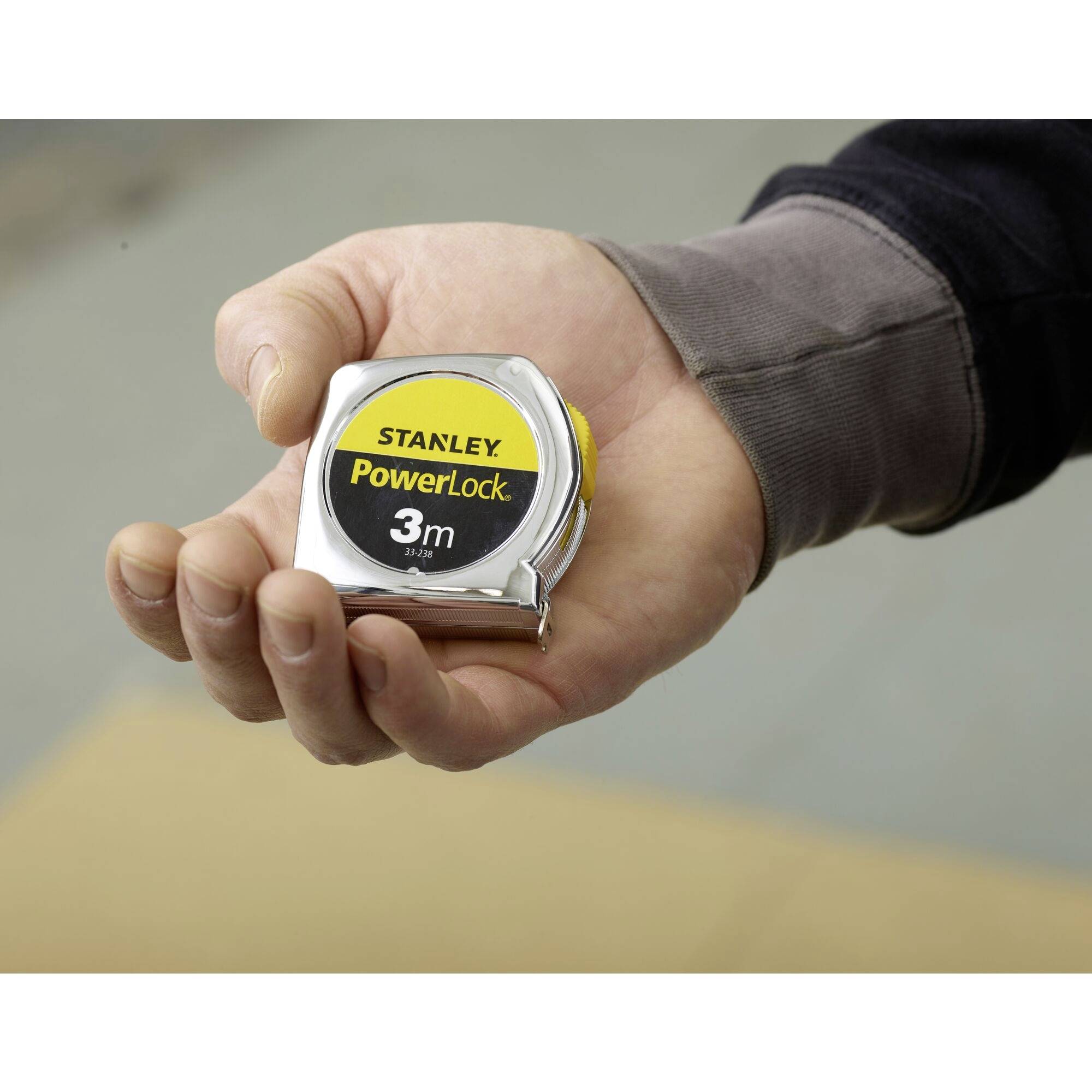 A hand is holding a tape measure with a 'Stanley PowerLock 3m' label. Use: Measuring distances.