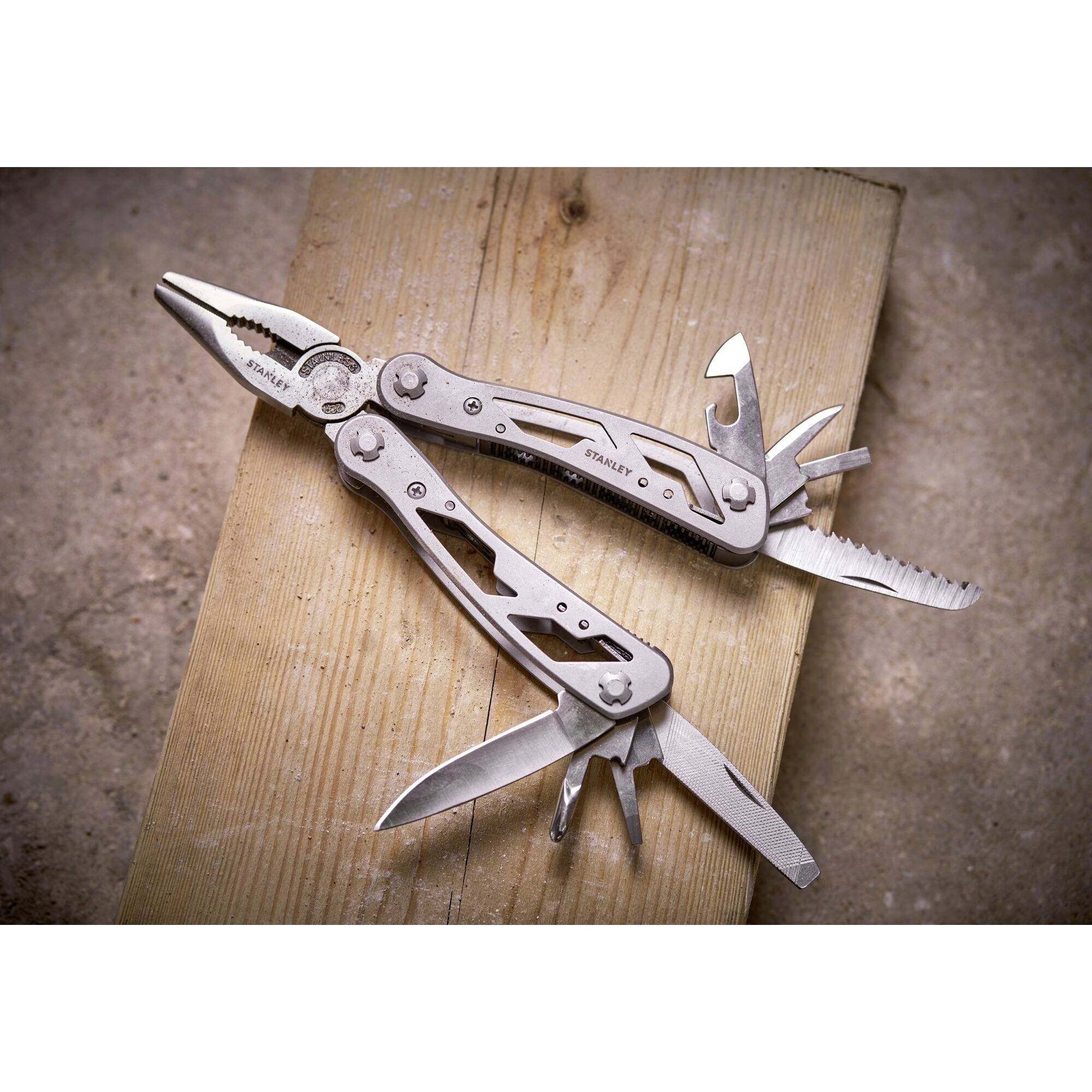 A silver multi-tool with pliers, knife and several other tools, lying on a wooden board.