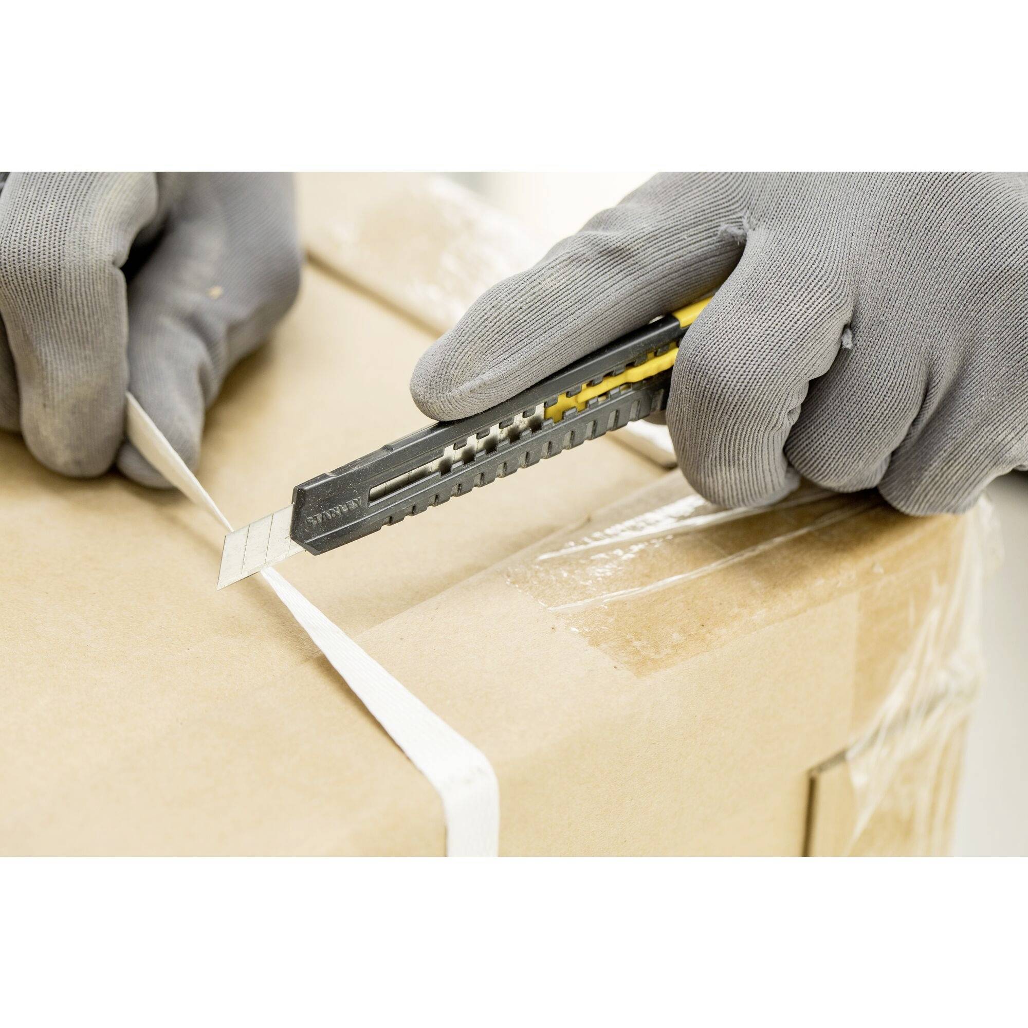 A person opens a cardboard box with a Stanley knife. They are wearing grey work gloves.