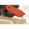 A hand wearing a black glove uses a red cutting tool to open a cardboard box.