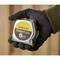 A gloved hand holds a Stanley brand tape measure with the inscription 'PowerLock 5m', against a blurred background.