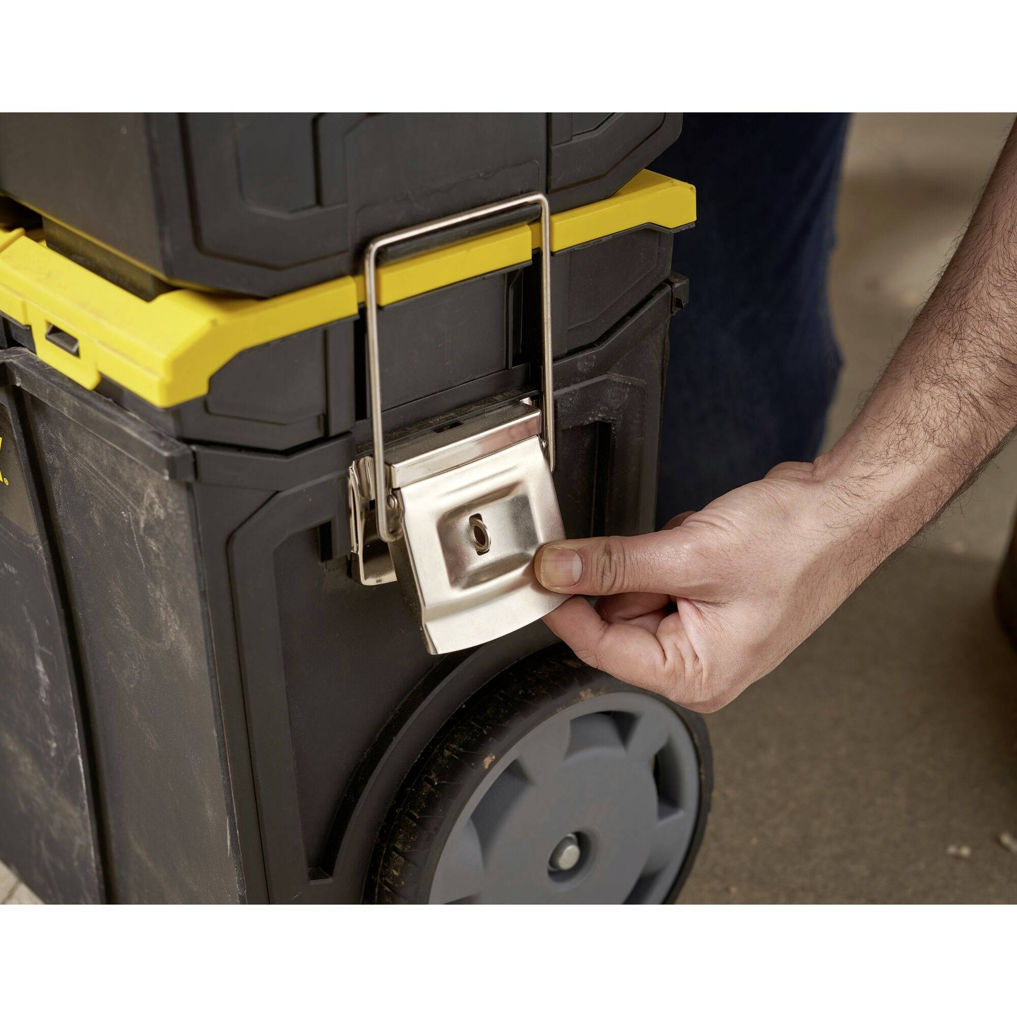 A person unlocks a toolbox with a metal padlock. The box has yellow and black elements and stands on wheels.