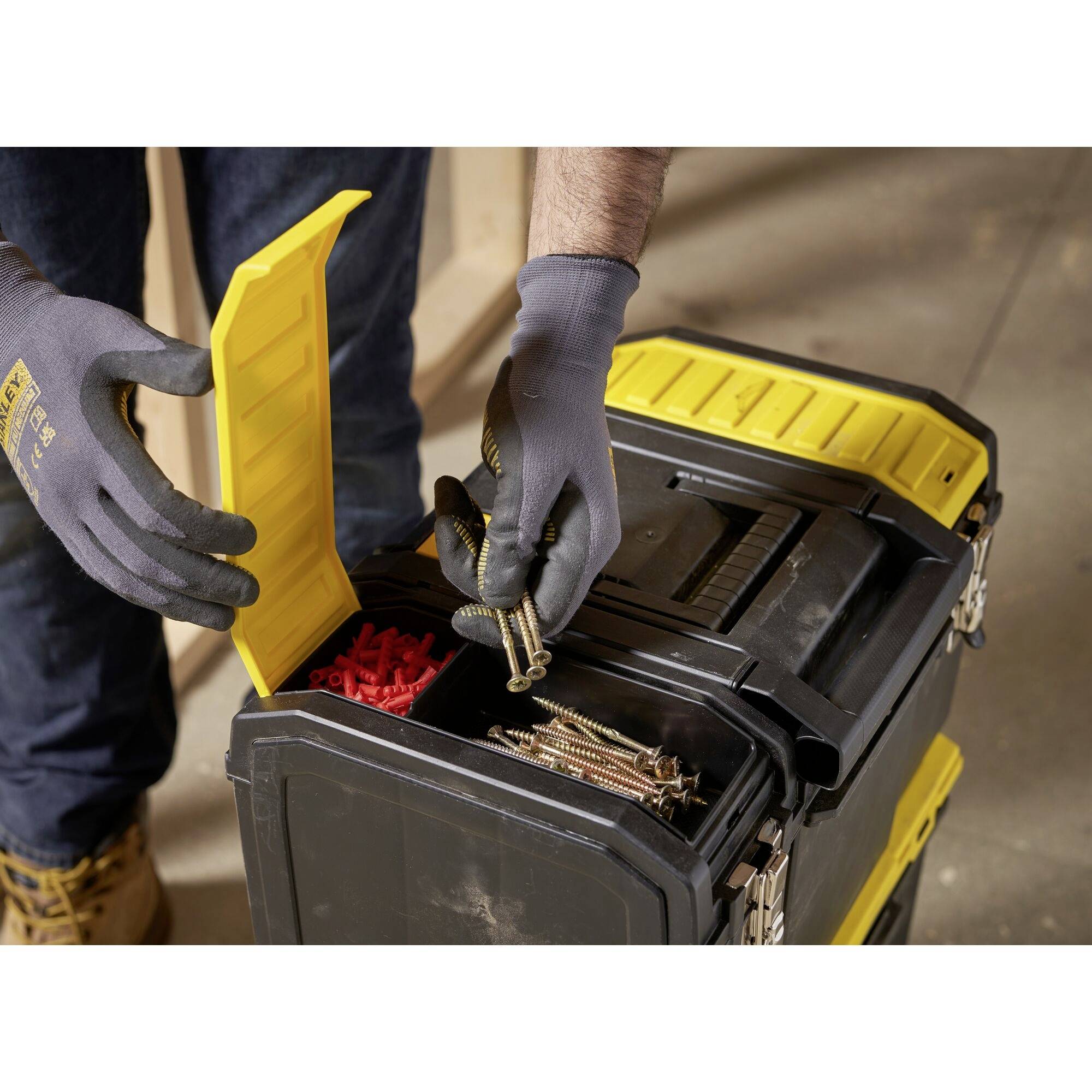A person is organising a toolbox with drawers. The box contains red plastic wall plugs and long gold-coloured screws.