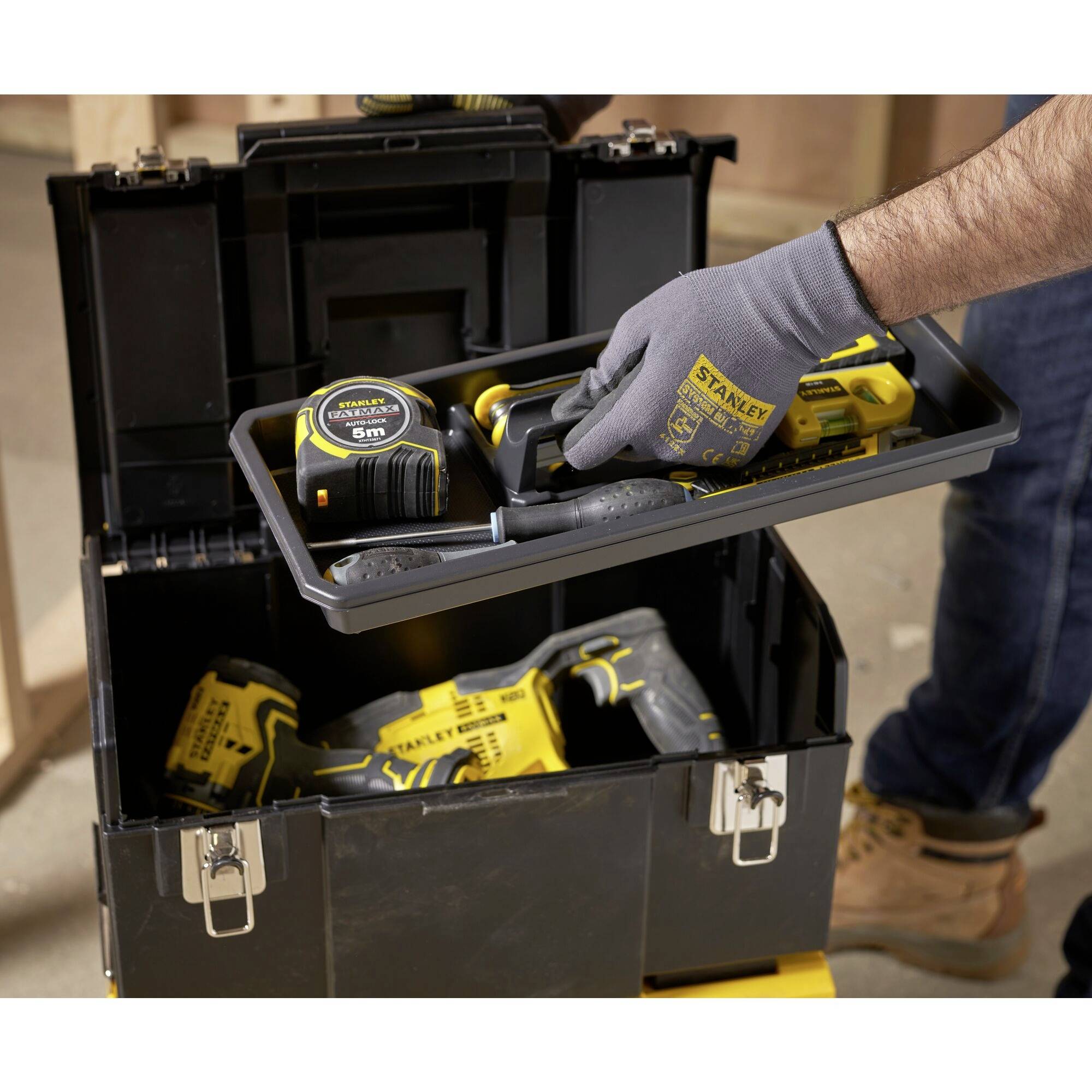 A person is arranging tools in an open toolbox. A tape measure, a spirit level, and yellow power tools are visible.