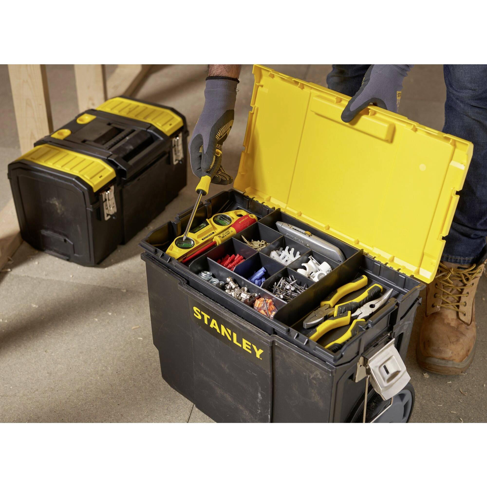 An open toolbox filled with sorted tools and small parts, with a person holding a screwdriver, and another toolbox in the background.