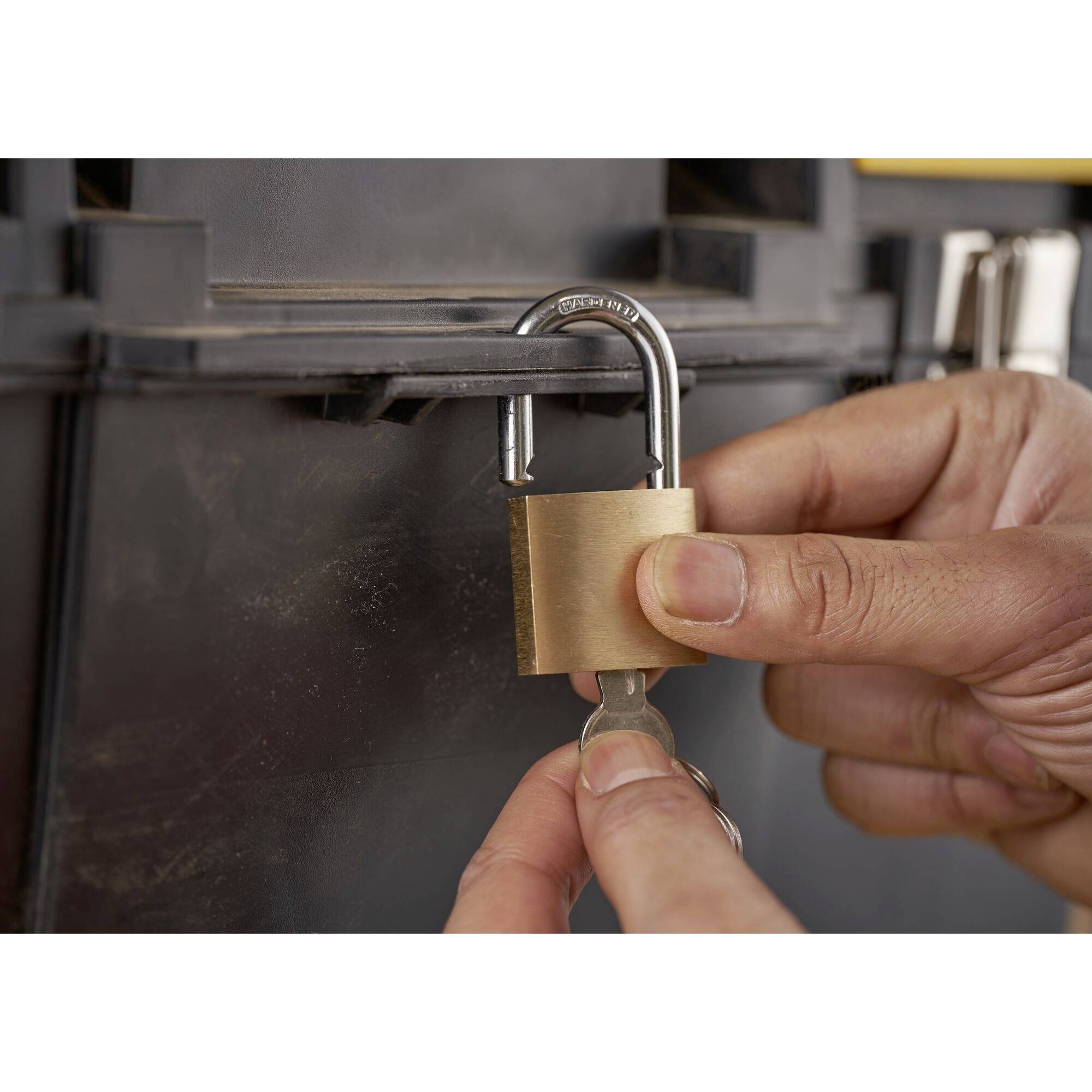A hand turns a key in a padlock attached to a metal box.