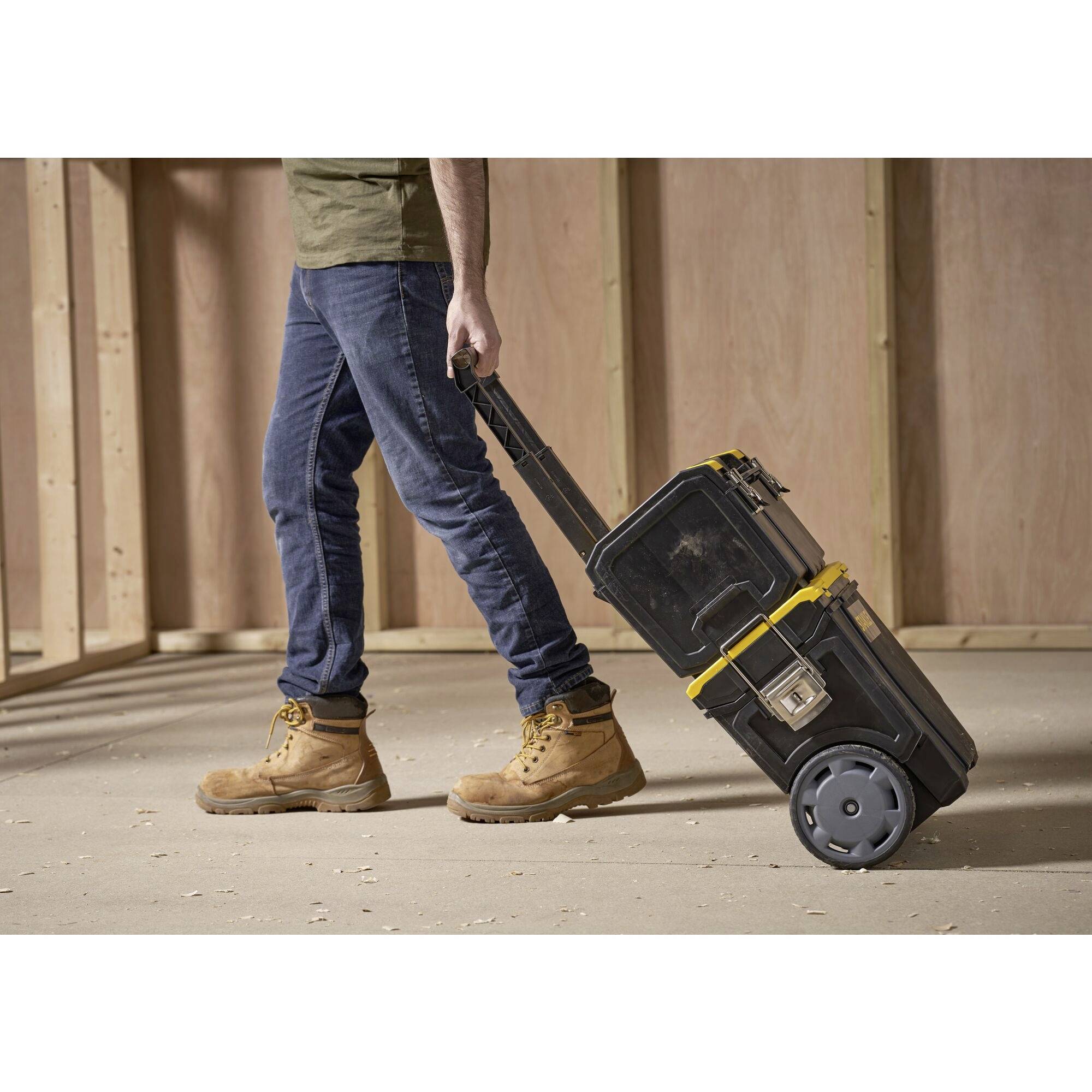 A person is pulling a wheeled toolbox on a construction site. The person is wearing jeans and sturdy boots.