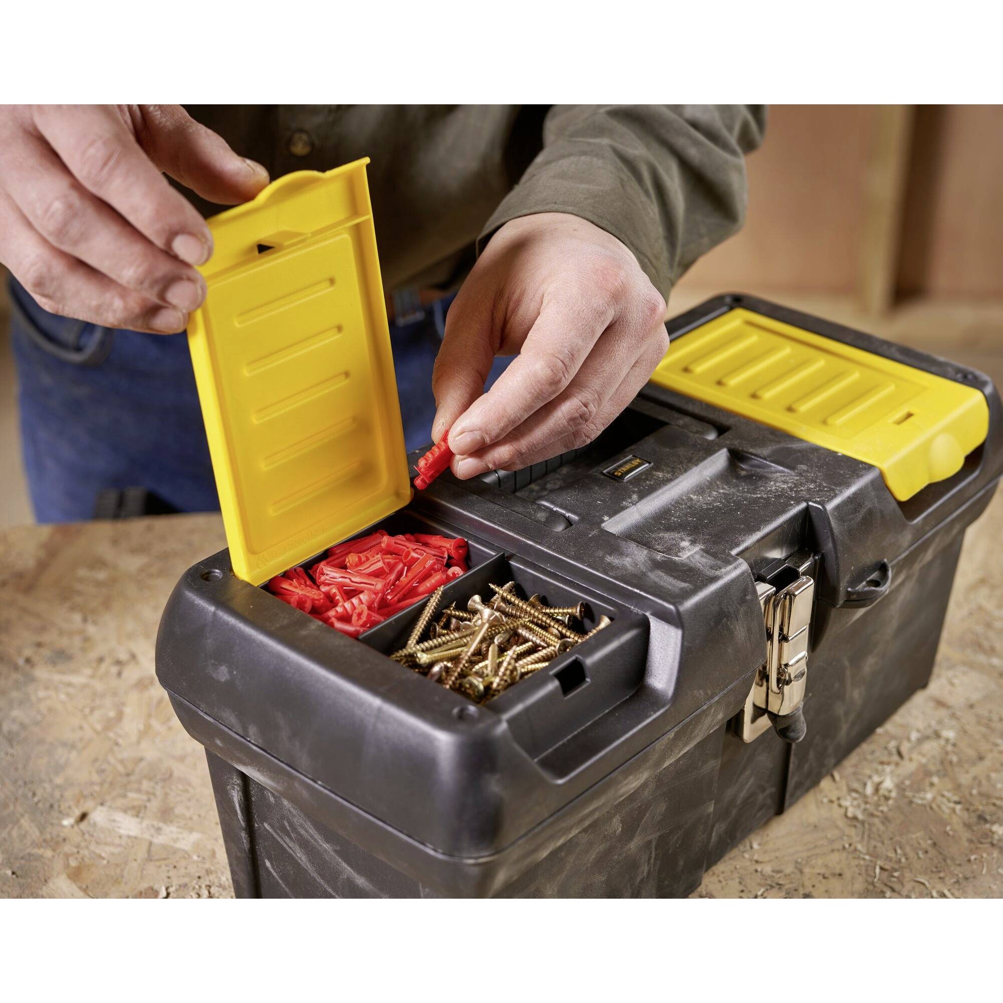 A person is placing red wall plugs into a toolbox. The box also contains screws and has a yellow lid.