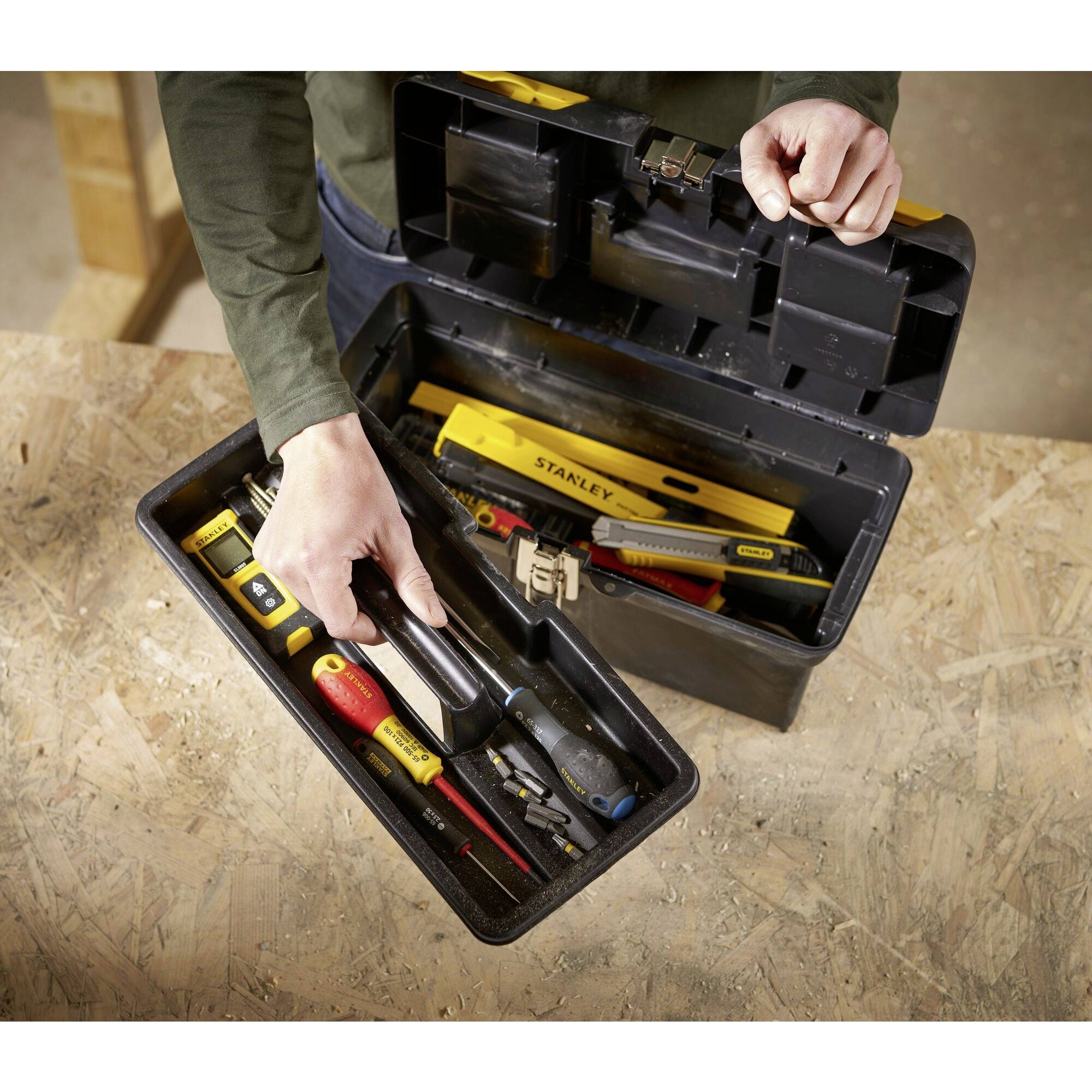 A person removes a screwdriver from a fully stocked toolbox, which is lying on a wooden table.