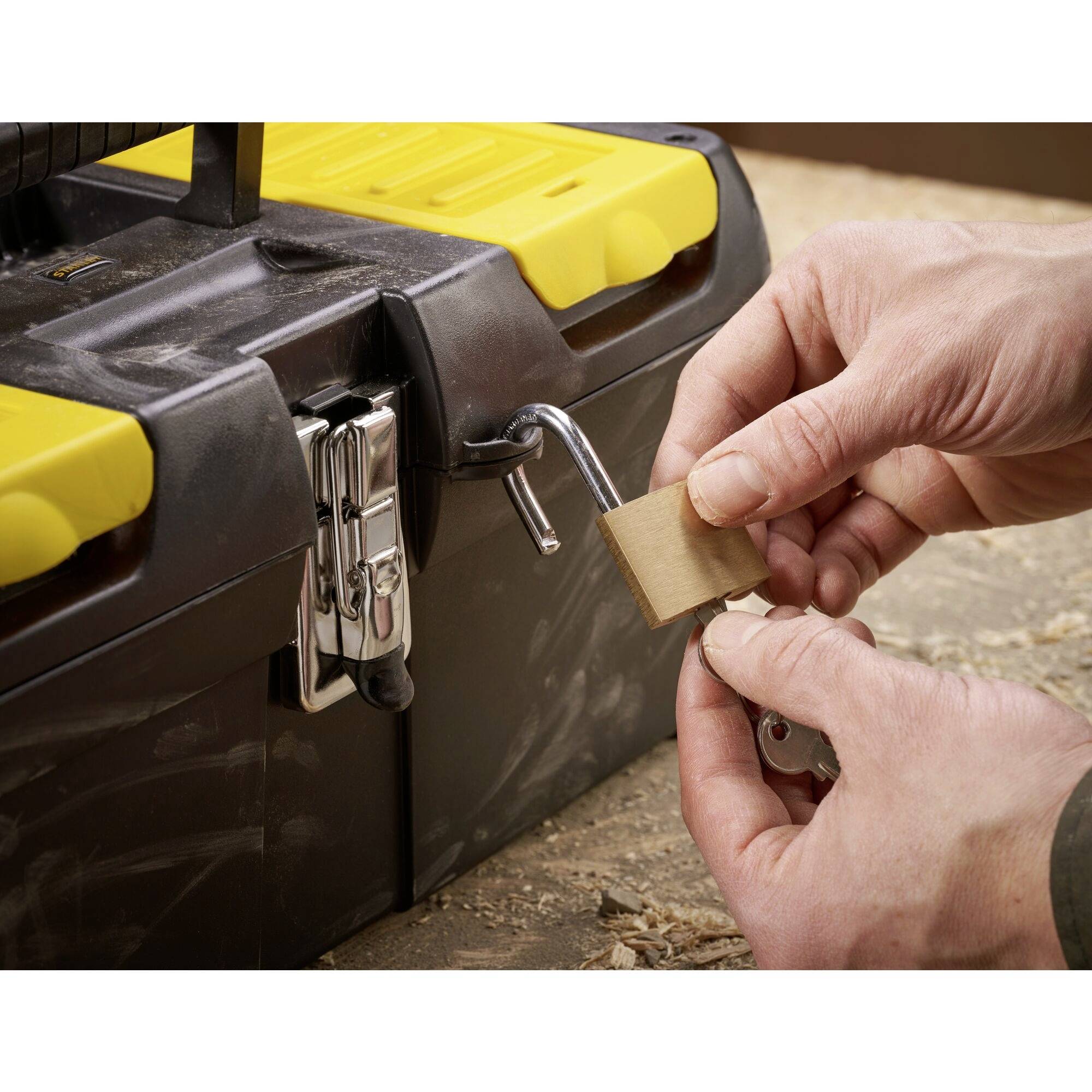 A person is sanding the shaft of a metal crank with sandpaper on a black toolbox with yellow accents.