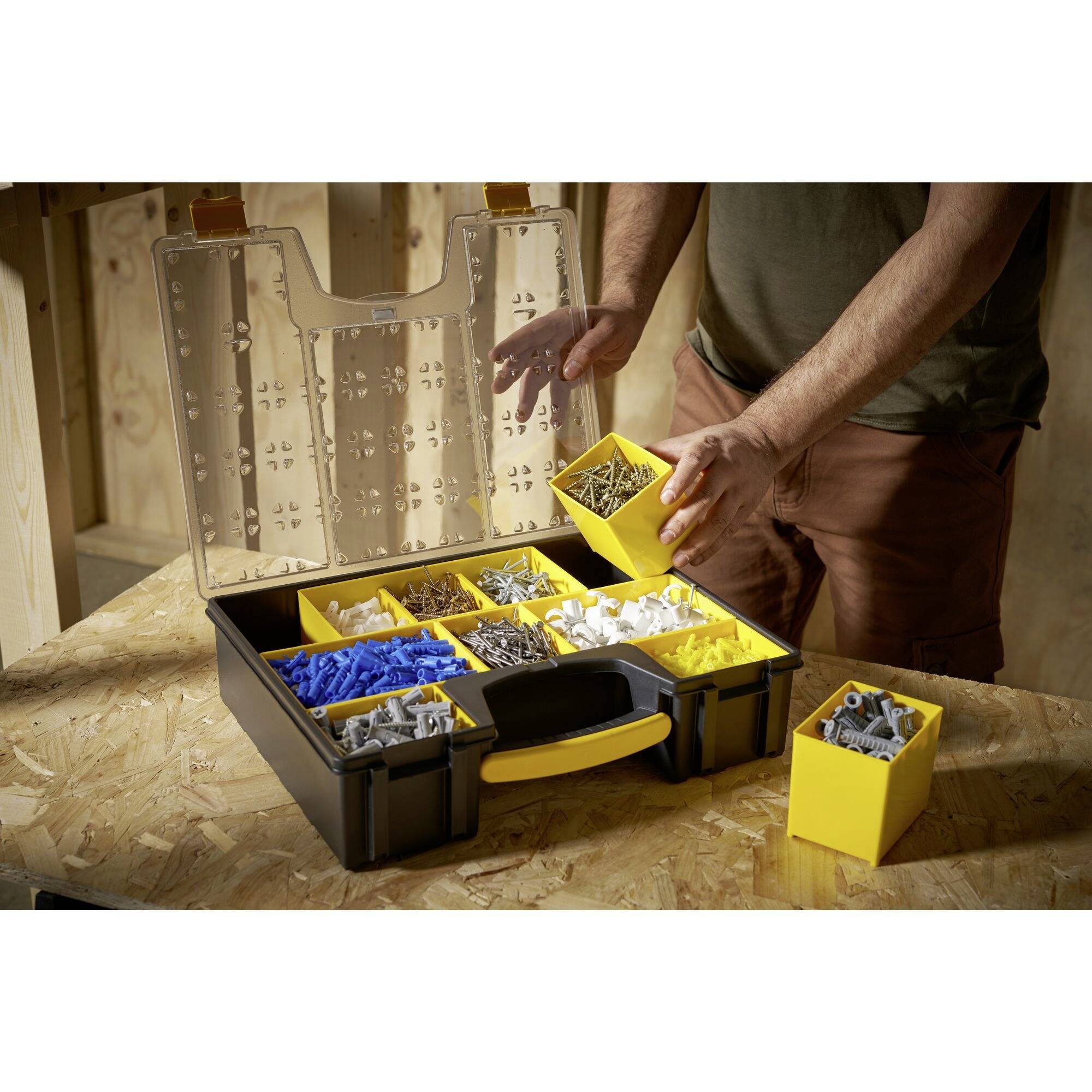 A person is organising screws and wall plugs in a black toolbox with yellow compartments. The box is sitting on a wooden table.