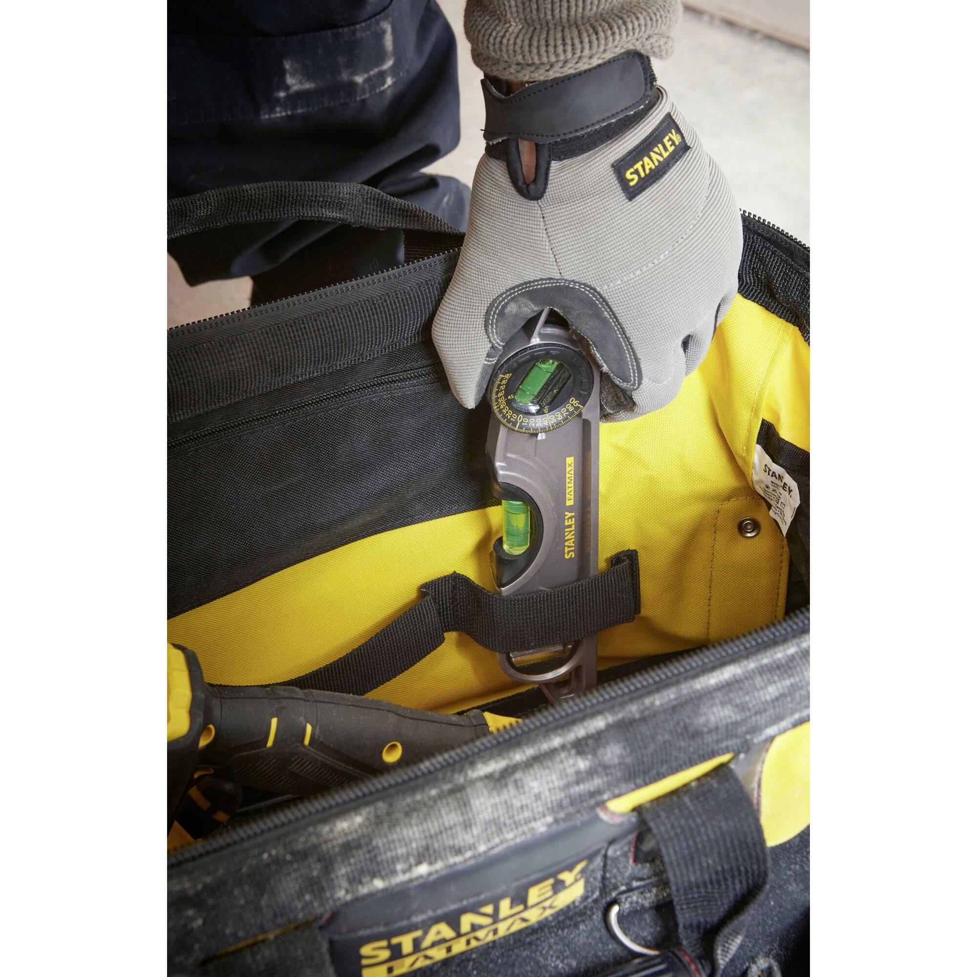 A person reaches into a Stanley toolbox and holds a Stanley tool with a green spirit level. The toolbox is black and yellow.