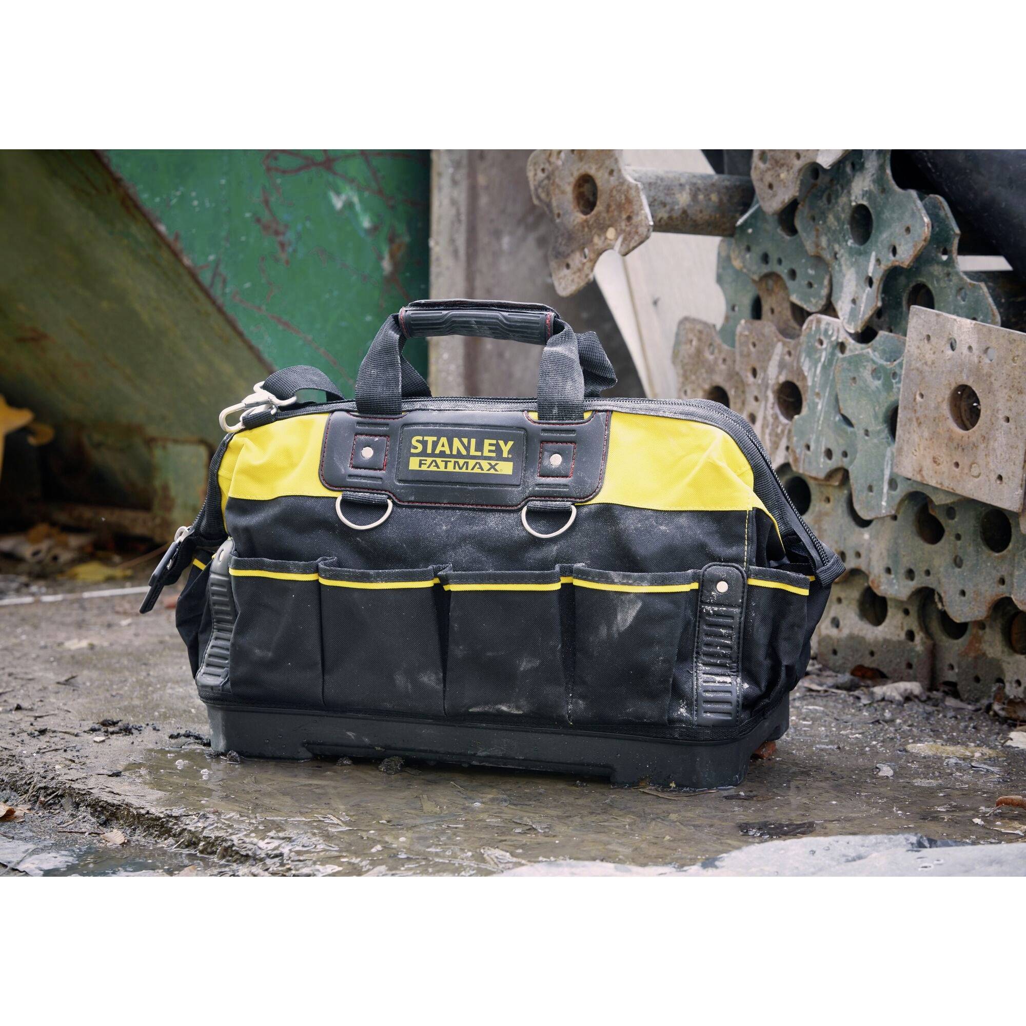 A black and yellow tool bag with the inscription 'Stanley Fatmax' is standing on a wet floor in front of a workshop wall.