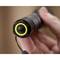 A thumb presses down on the yellow button of a black torch. Focus on the non-slip grip and the hand holding the device.