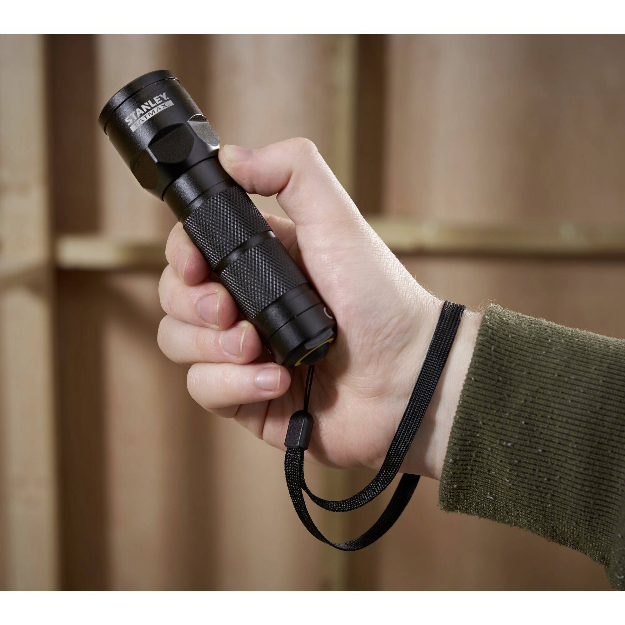 A hand is holding a small torch with a black casing. Blurred wooden beams are visible in the background.