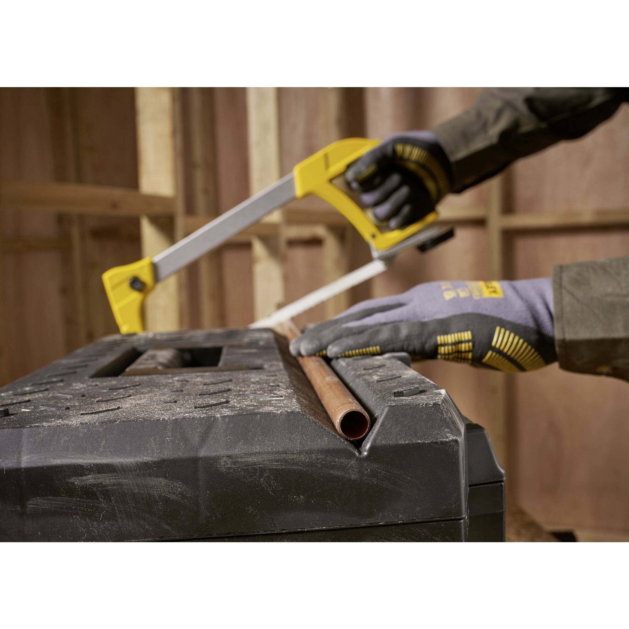 A person is sawing a copper pipe with a handsaw in a workshop. The person is wearing safety gloves.
