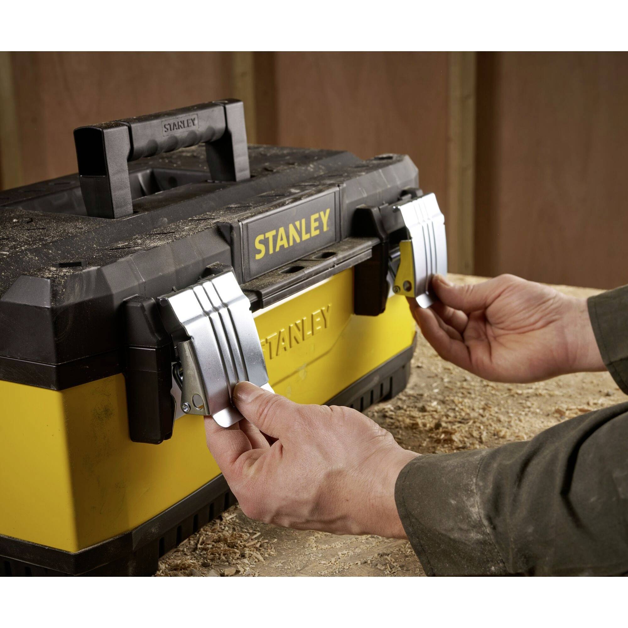 A person opens a yellow toolbox with two silver latches in a workshop environment.