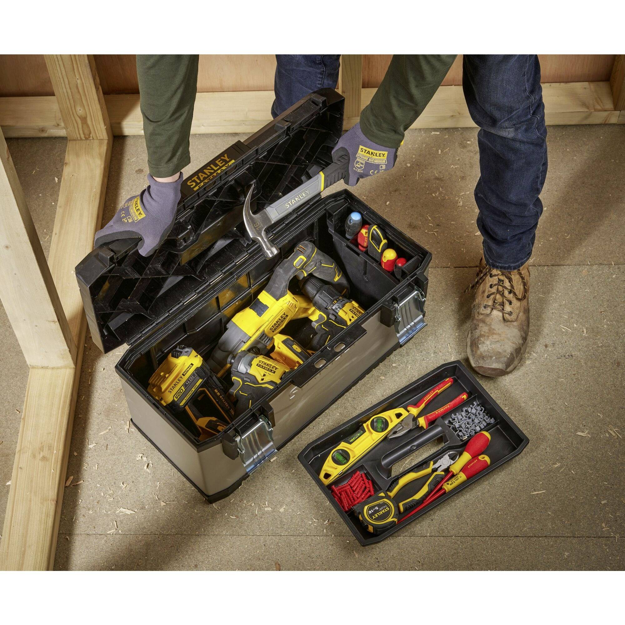 An open toolbox on the floor displays various tools, including drills, screwdrivers and a hammer. A person reaches inside.