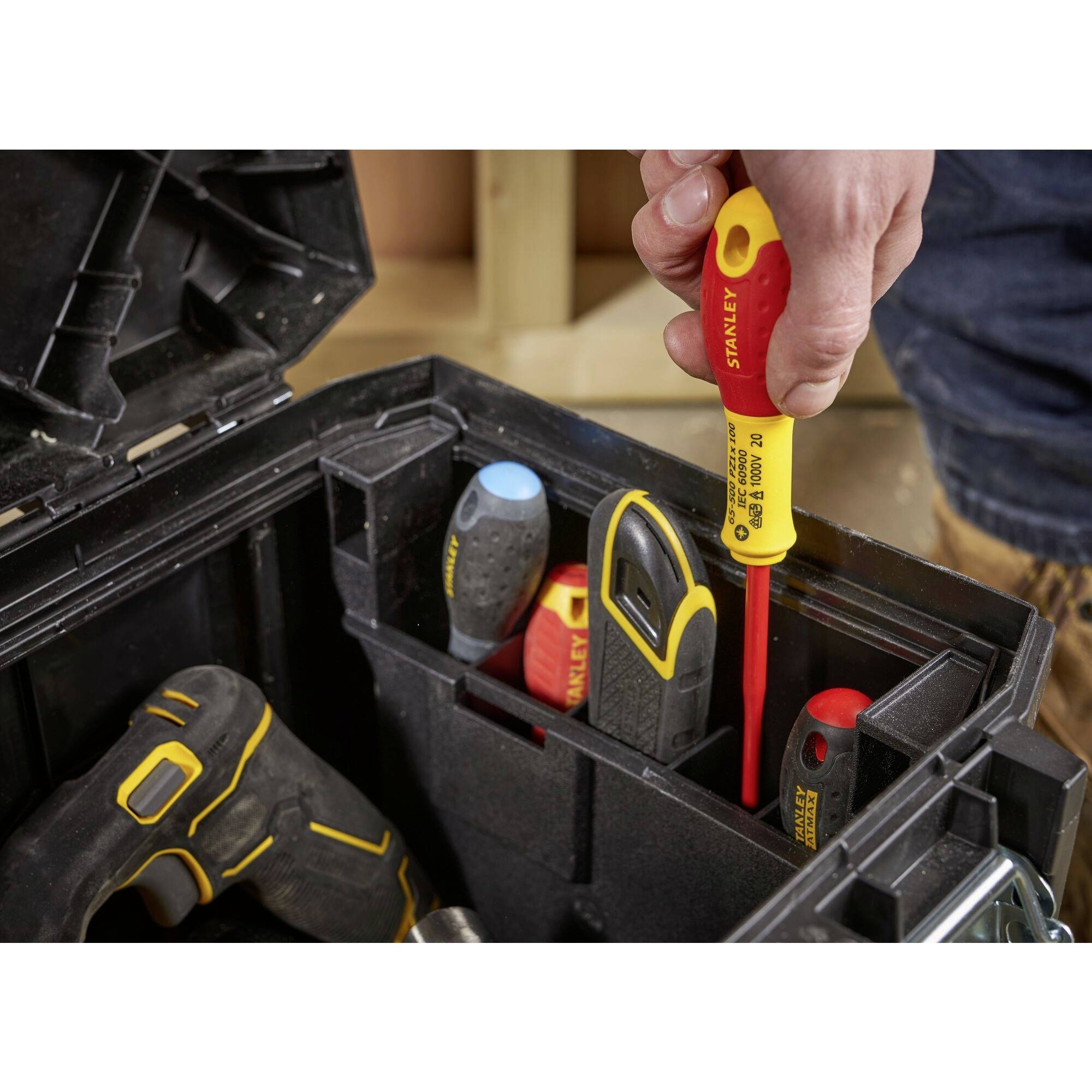 A toolbox with various screwdrivers and a power drill. A hand is holding a red screwdriver.