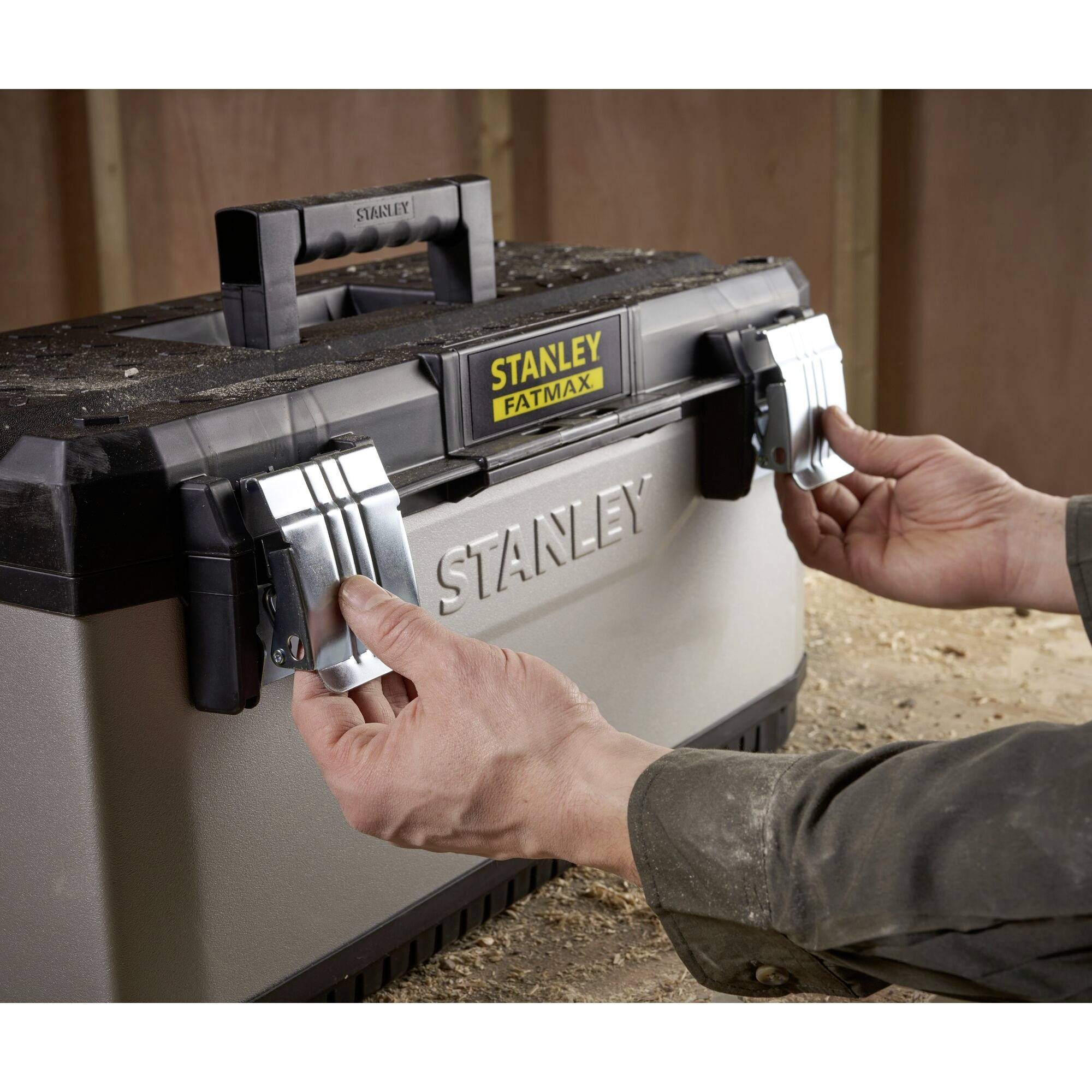 A person opens a large silver Stanley Fatmax toolbox in a workshop environment.
