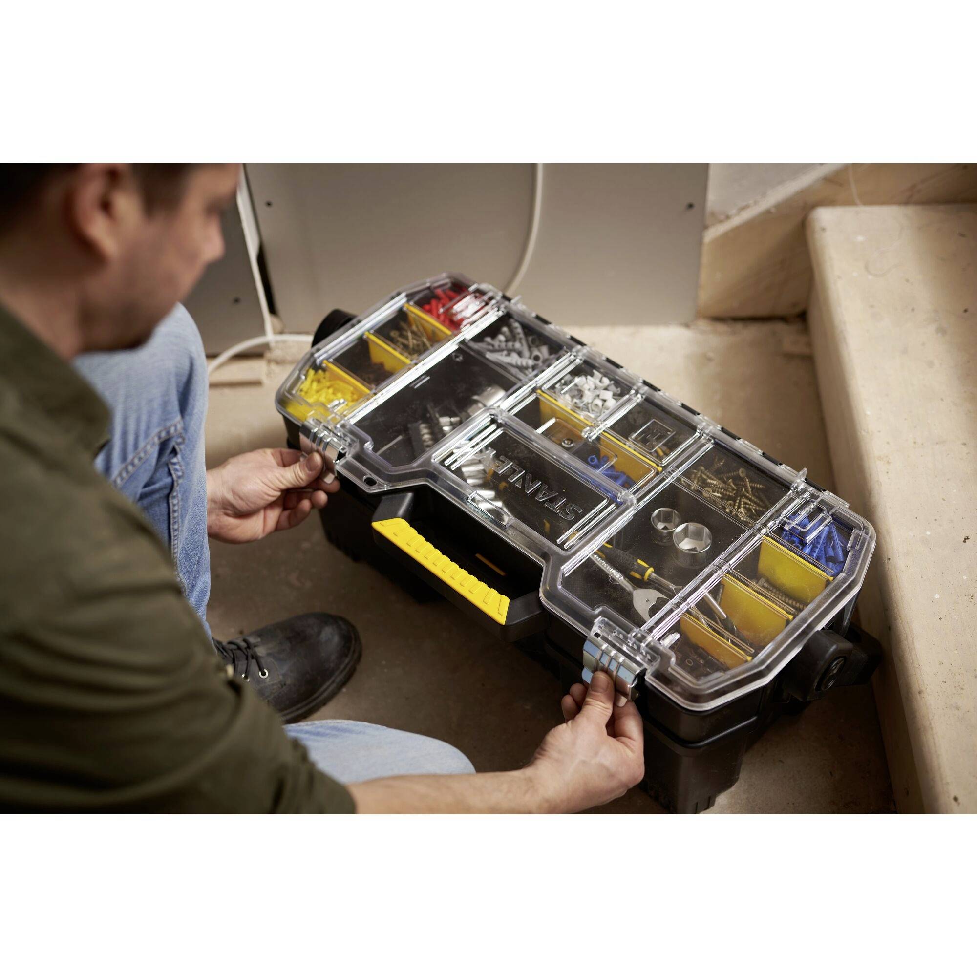 A man kneels before a folding toolbox with a transparent lid and various compartments for screws and accessories.