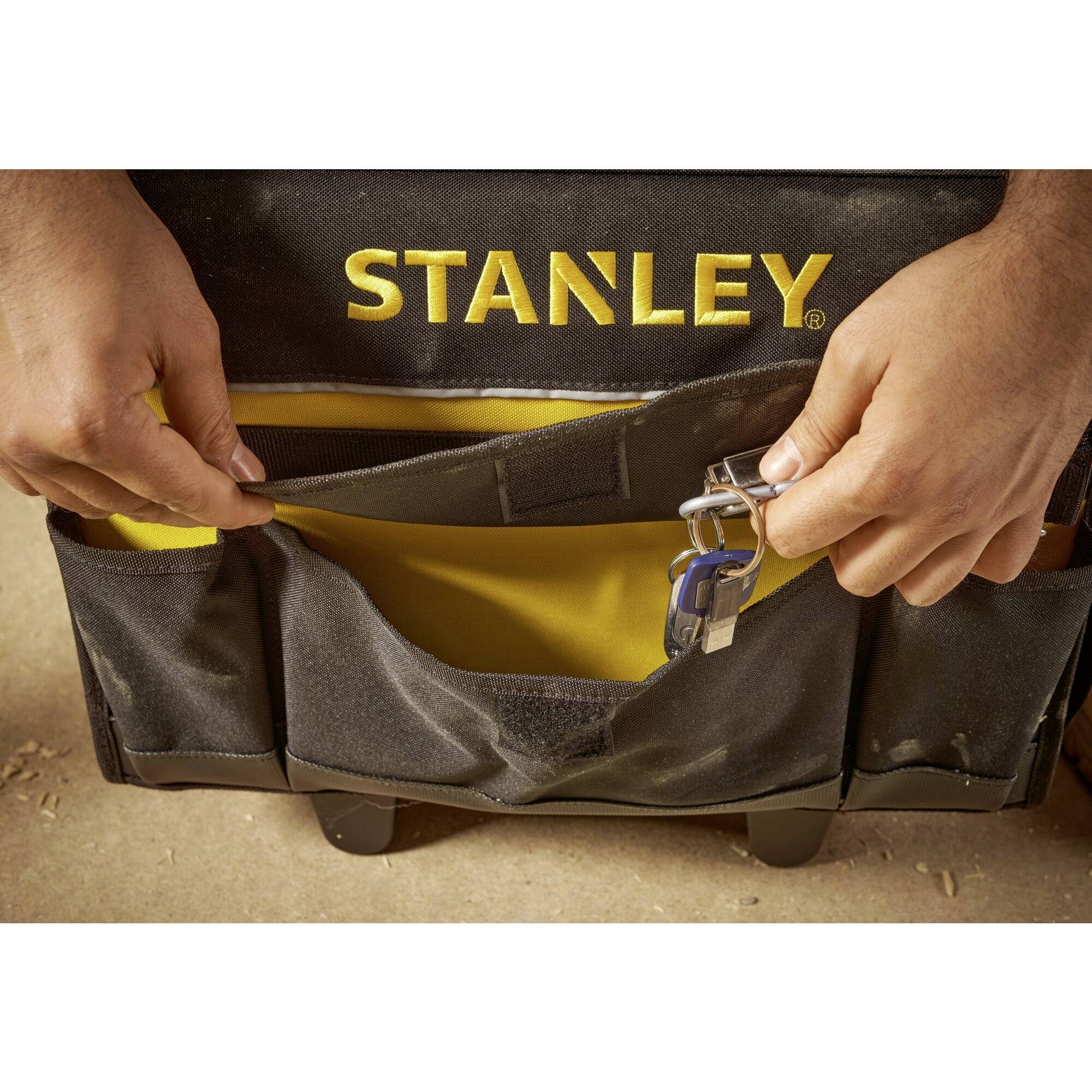 A person is holding a black tool bag with a yellow logo. The bags are open, revealing a spanner and other tools.