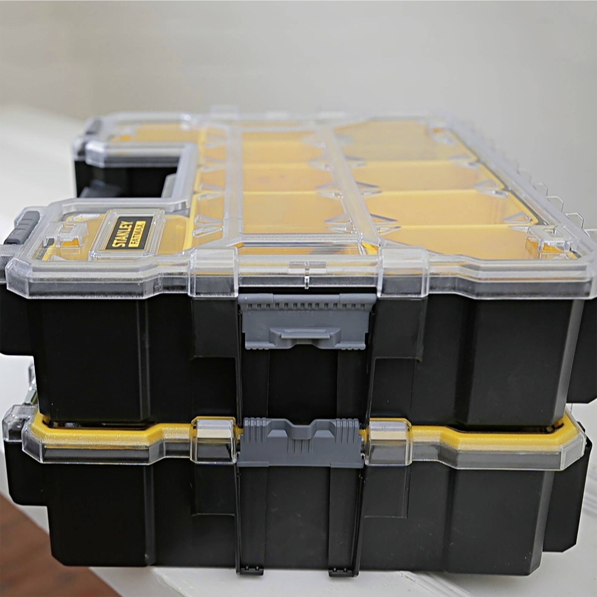 Black tool case with transparent lid on white table; multiple yellow compartments for small parts; portable organiser.