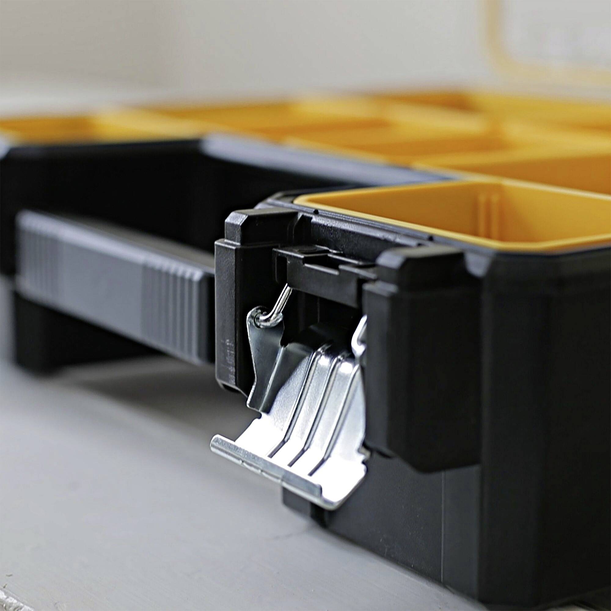 A black toolbox with yellow compartments is sitting on a table. The lid is open, revealing its internal structure.