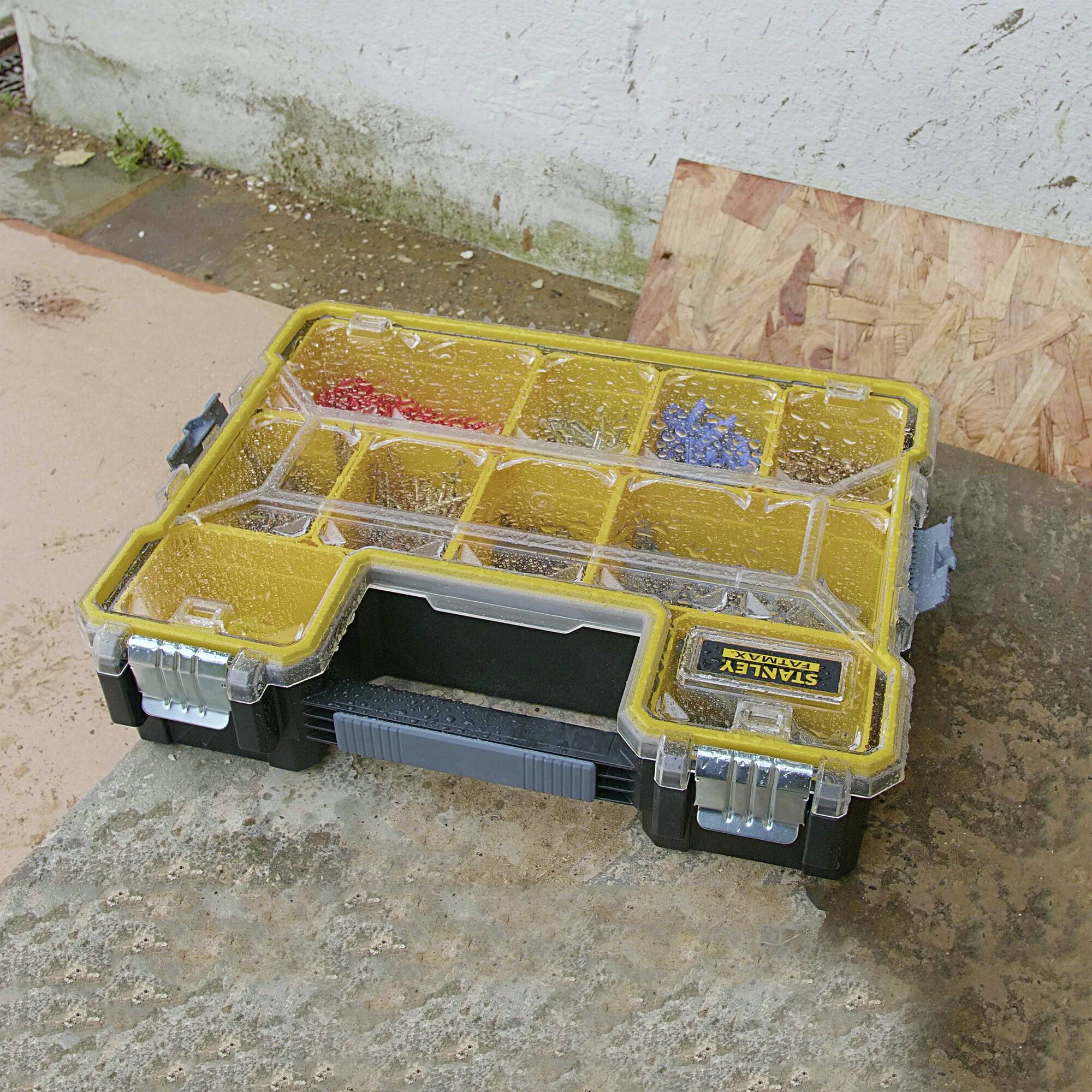 An open toolbox with compartments containing various screws and nuts lies outdoors on a stone surface.