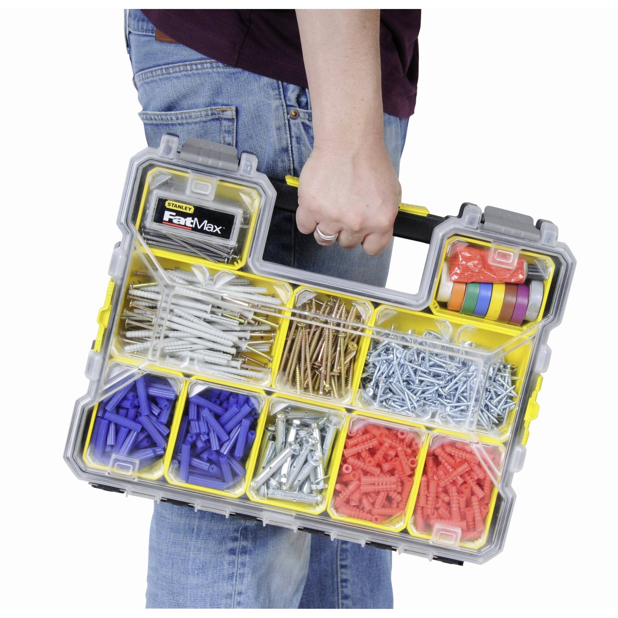 A person is carrying a yellow toolbox with multiple compartments containing various screws, wall plugs, and adhesive tapes.