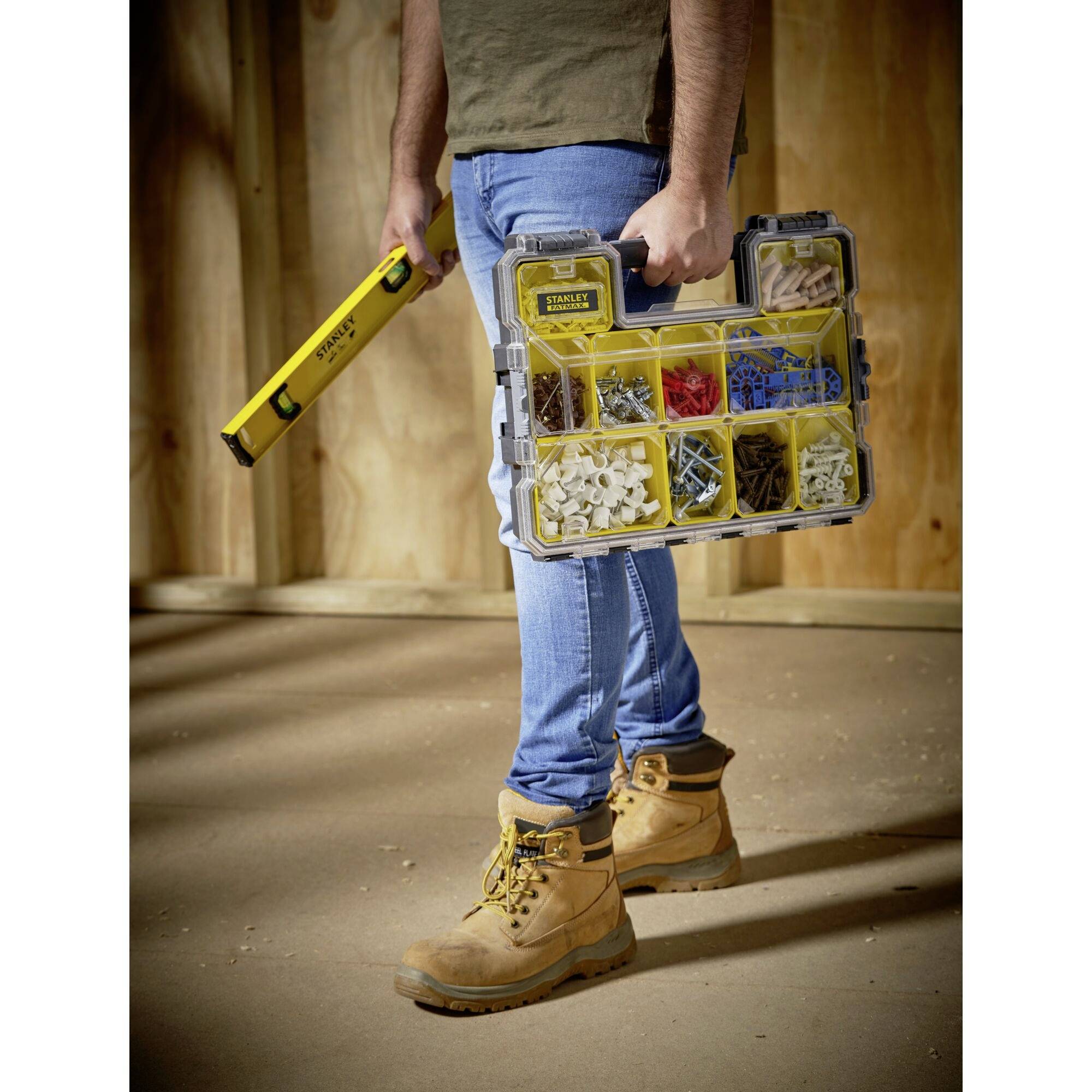 A person is holding a toolbox with various screws and wall plugs in a partially completed room. They are wearing construction clothing.