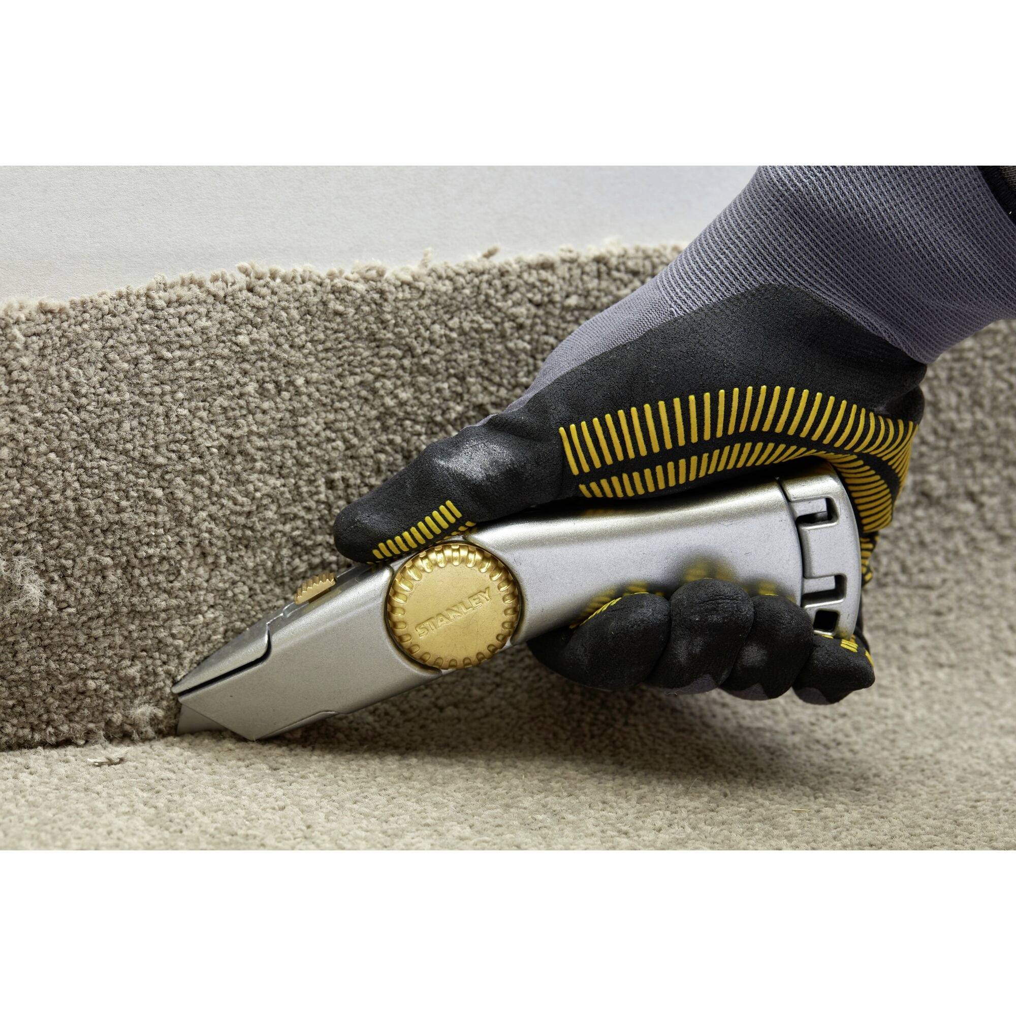 A tradesman wearing protective gloves is cutting a carpet with a utility knife.