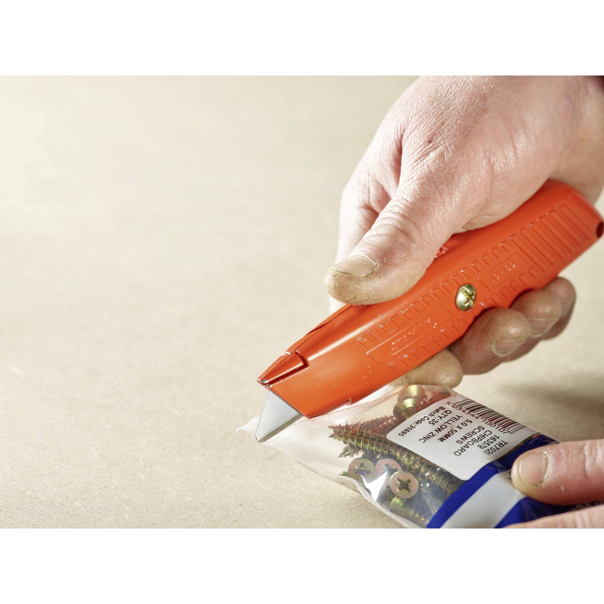 A hand is using an orange cardboard opener to open a plastic packaging containing screws.