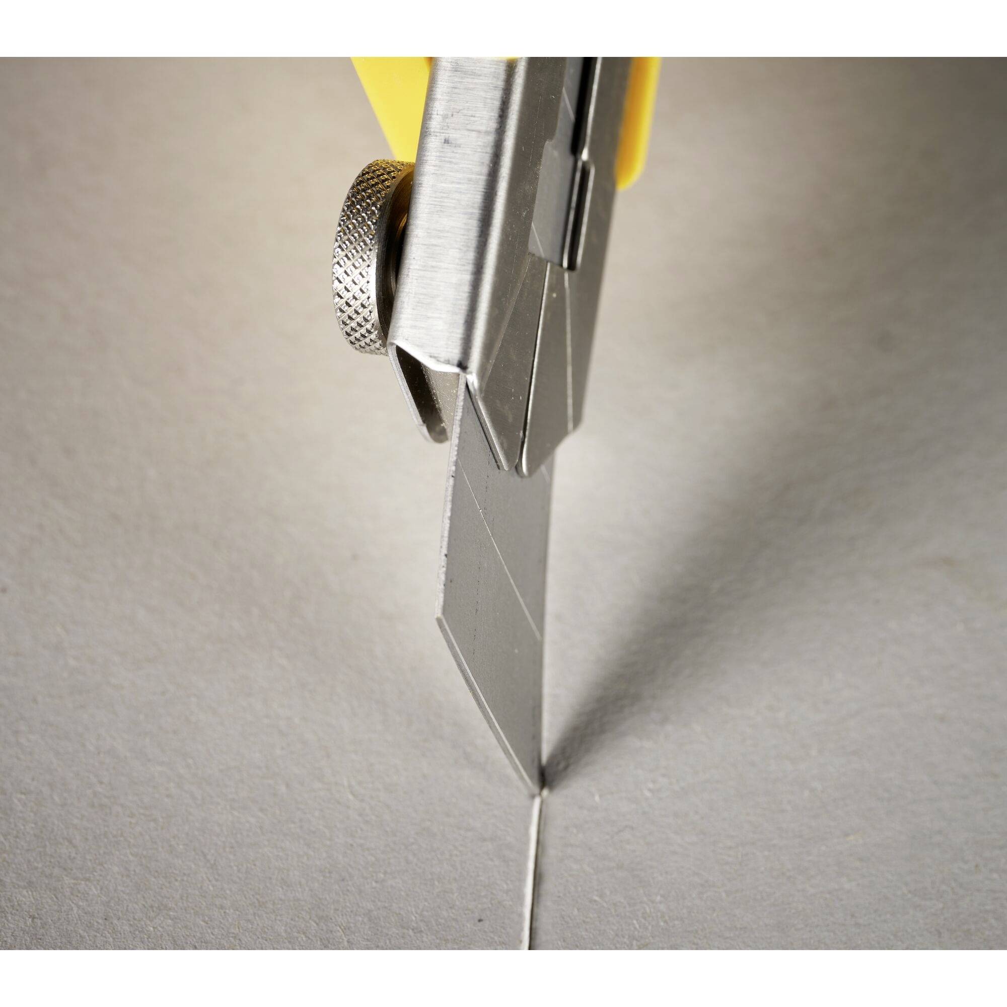 A craft knife precisely cuts through grey cardboard, close-up of the blade in action.