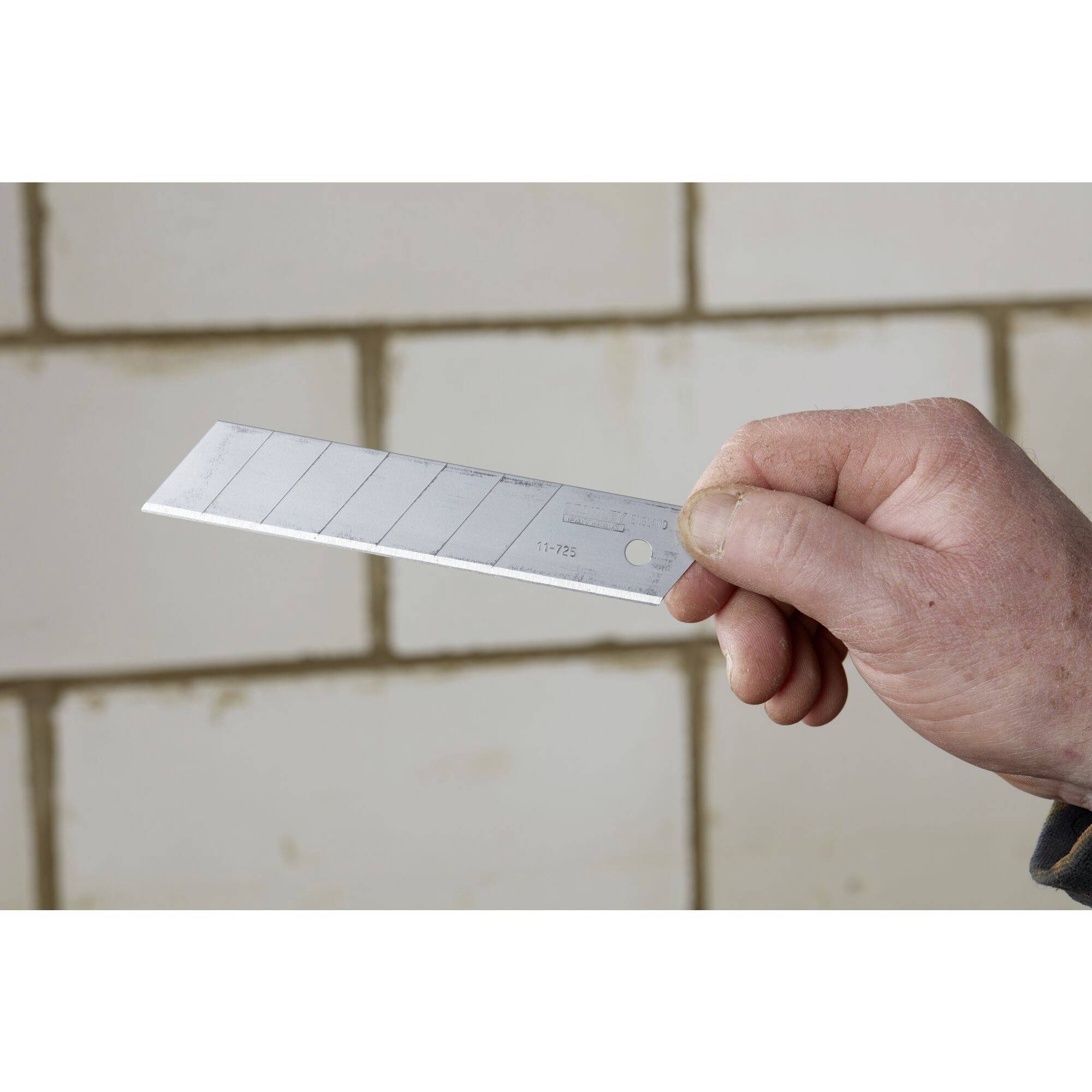 A hand is holding a snap-off blade knife in front of a wall with white, square tiles.