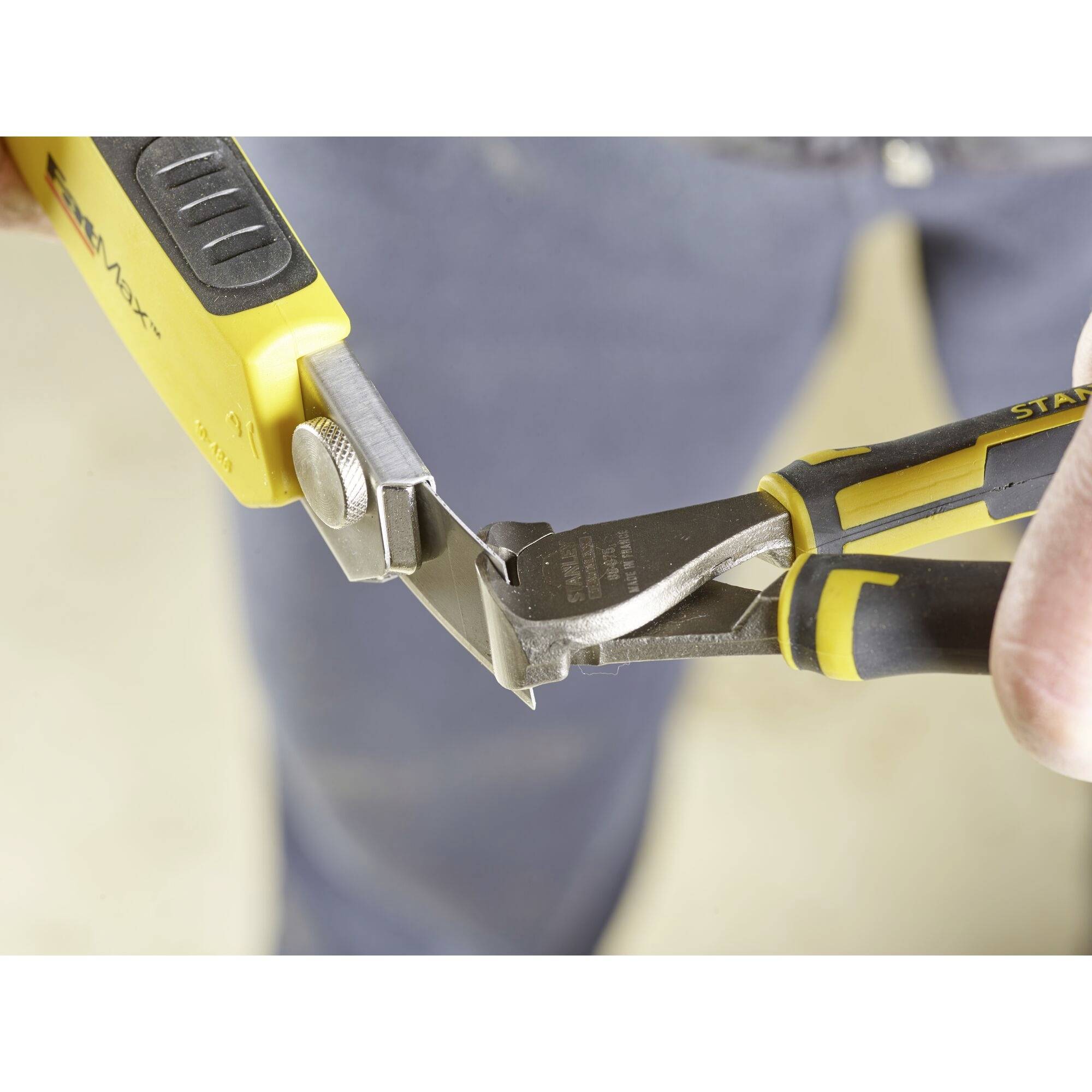 A person is using a yellow and black side cutters to work on a workpiece. The focus is on the tool.