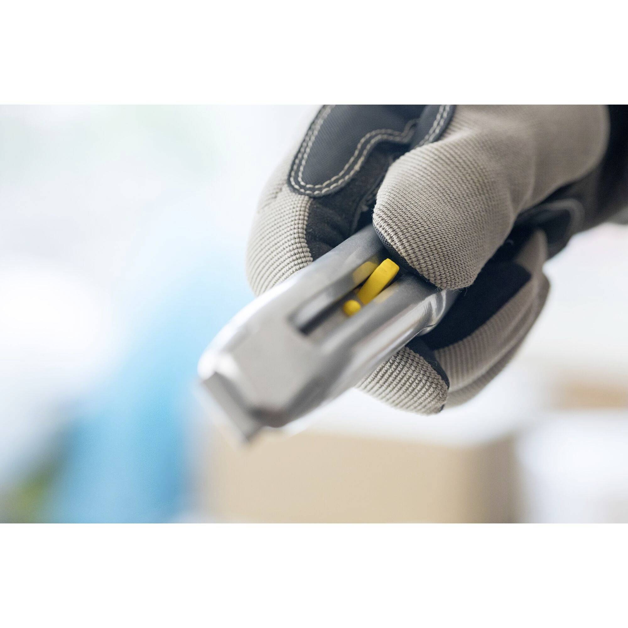 A hand wearing a grey glove holds a silver, rectangular object with a yellow detail. Background is blurred.