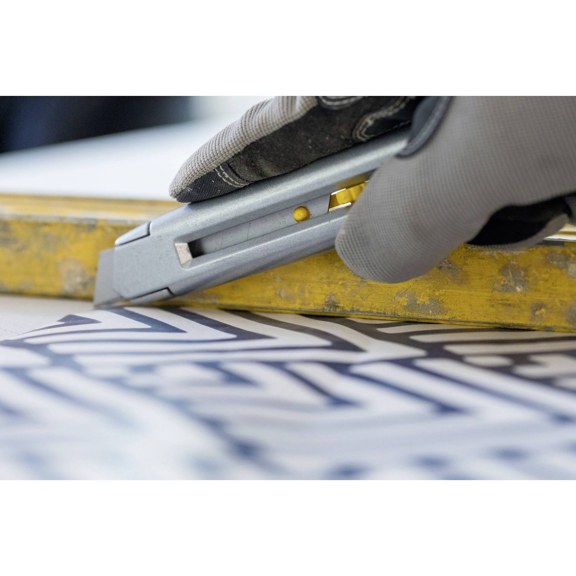 A hand wearing a glove uses a craft knife to cut a piece of paper with a geometric pattern on a yellow ruler.
