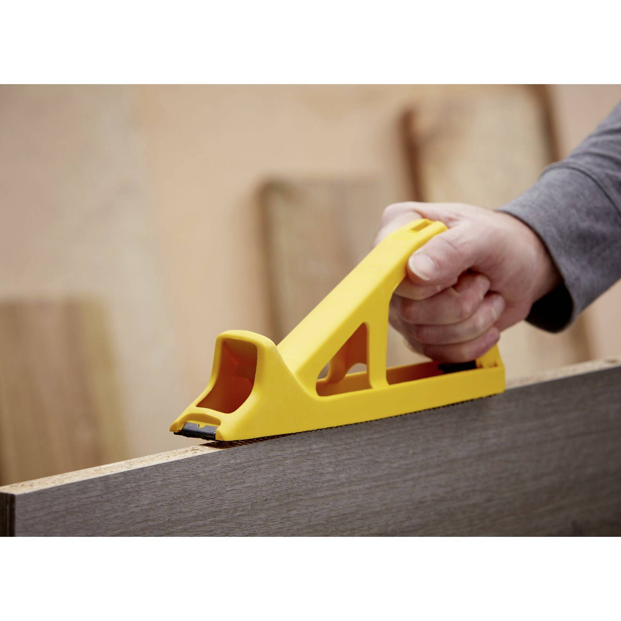 A hand is using a yellow sanding block to smooth a wooden board. Further wooden boards can be seen in the background.