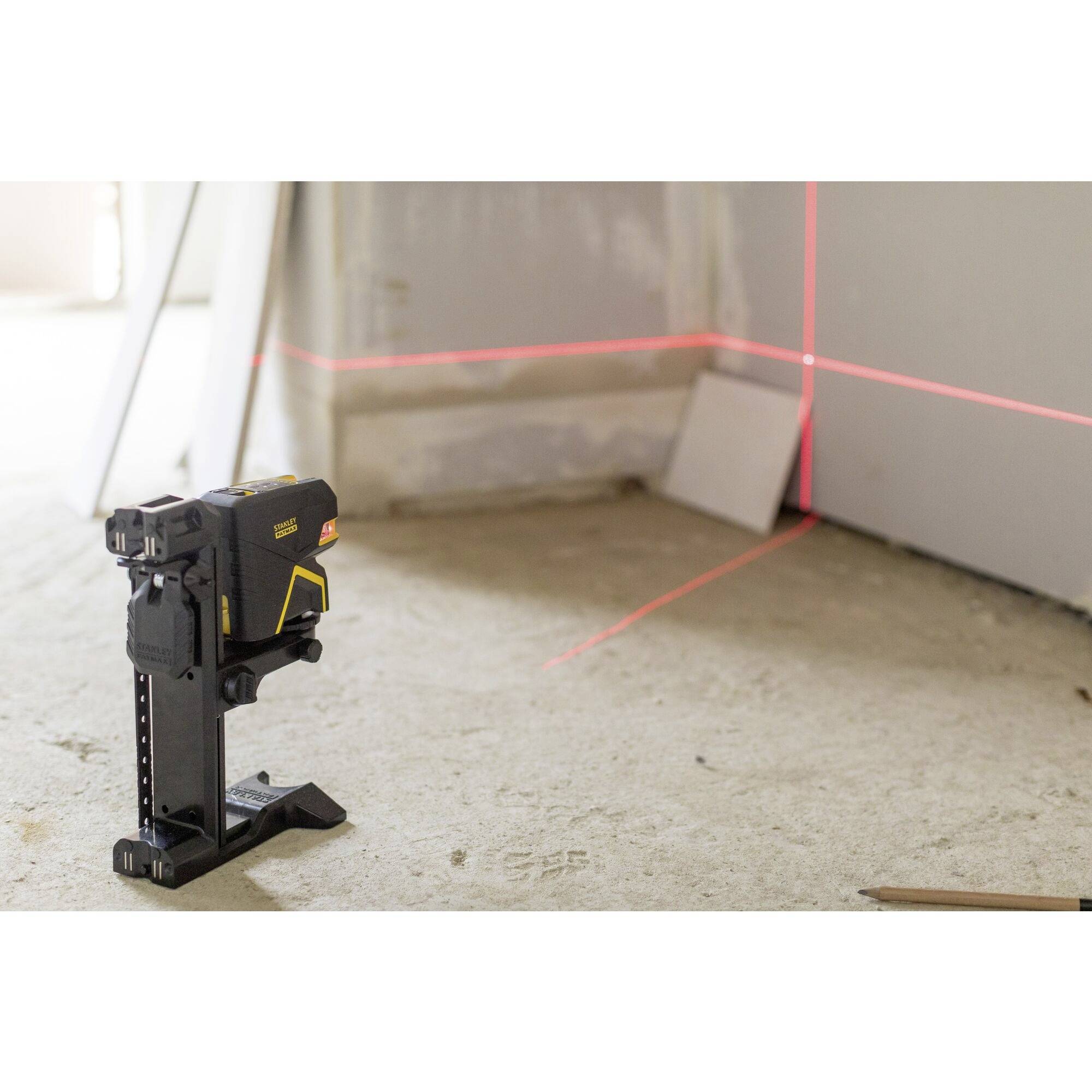 A laser levelling device projects red lines onto a wall and floor in a room to carry out precise measurements.
